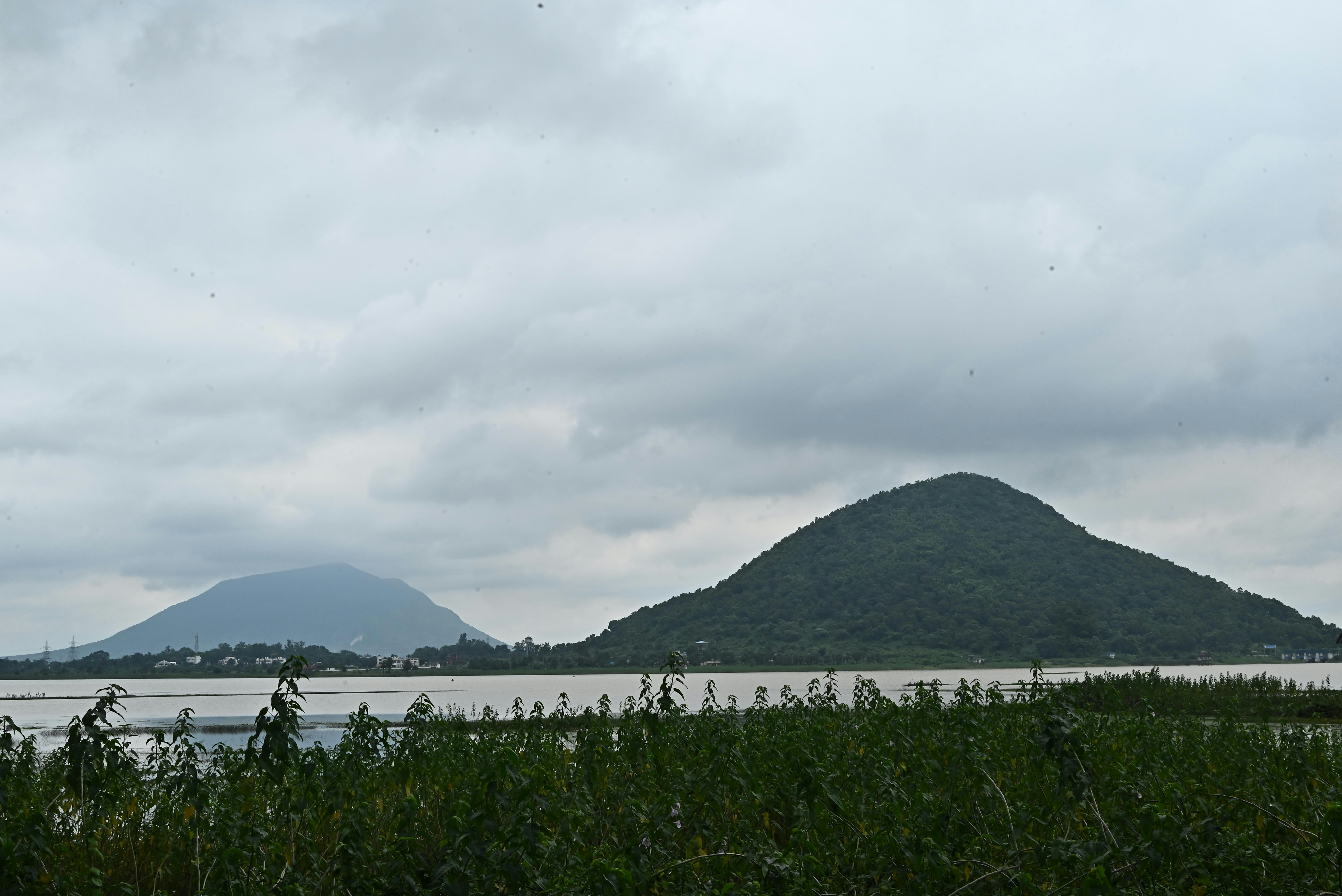 Two green hills rising above a calm lake under a cloudy sky