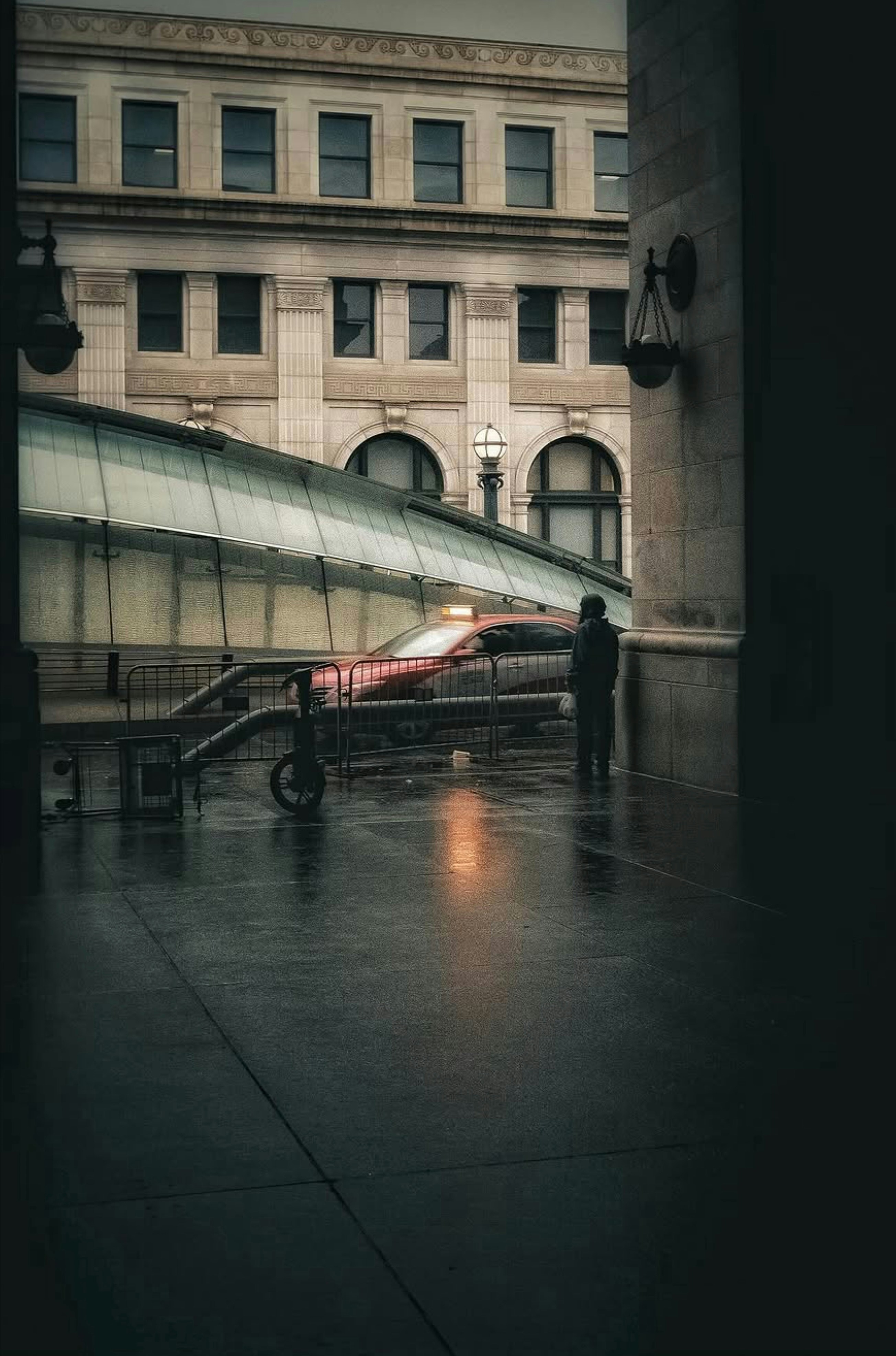 A person in a dark coat on a wet city sidewalk near a taxi