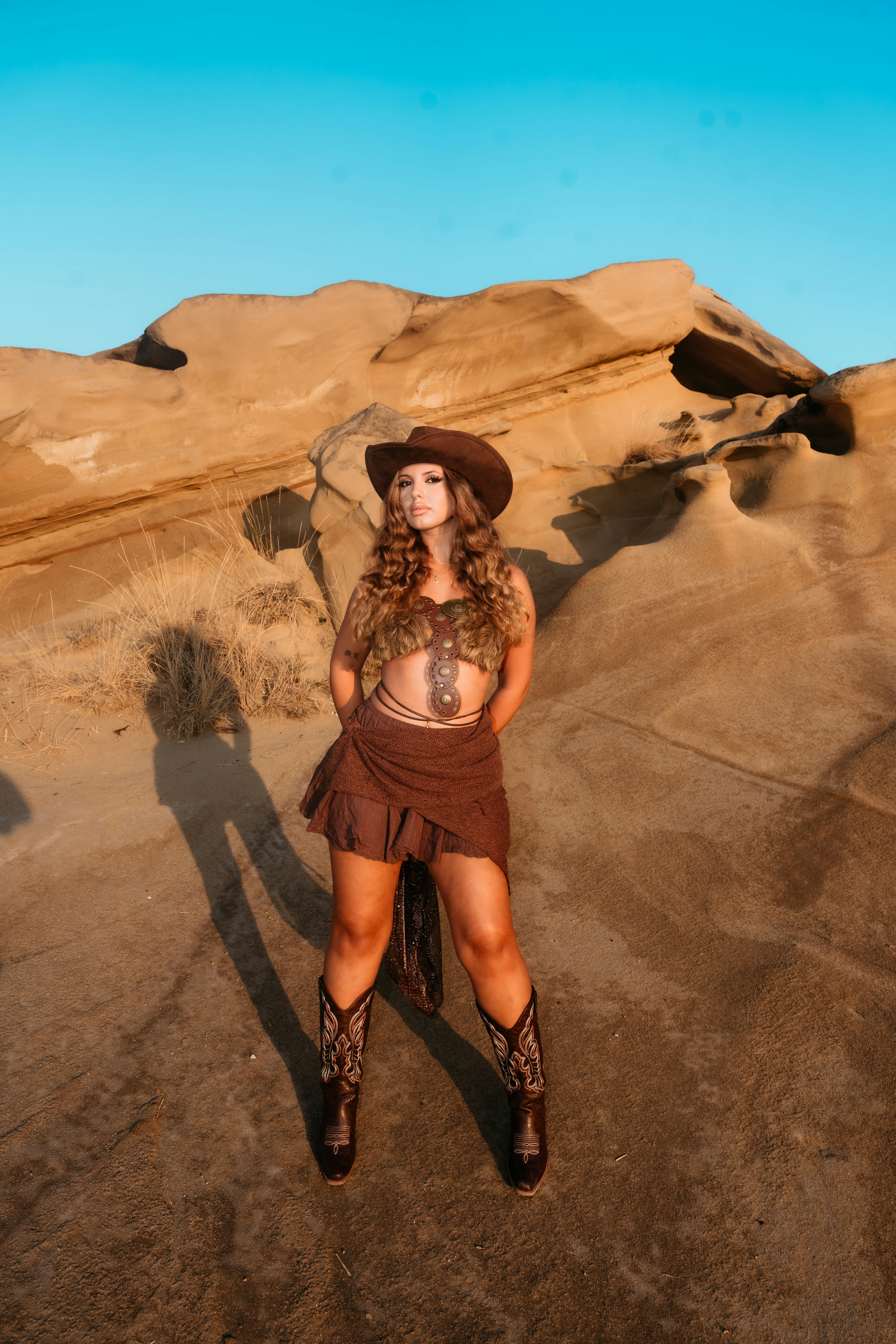 A woman in a brown cowboy hat and boots standing in a desert landscape