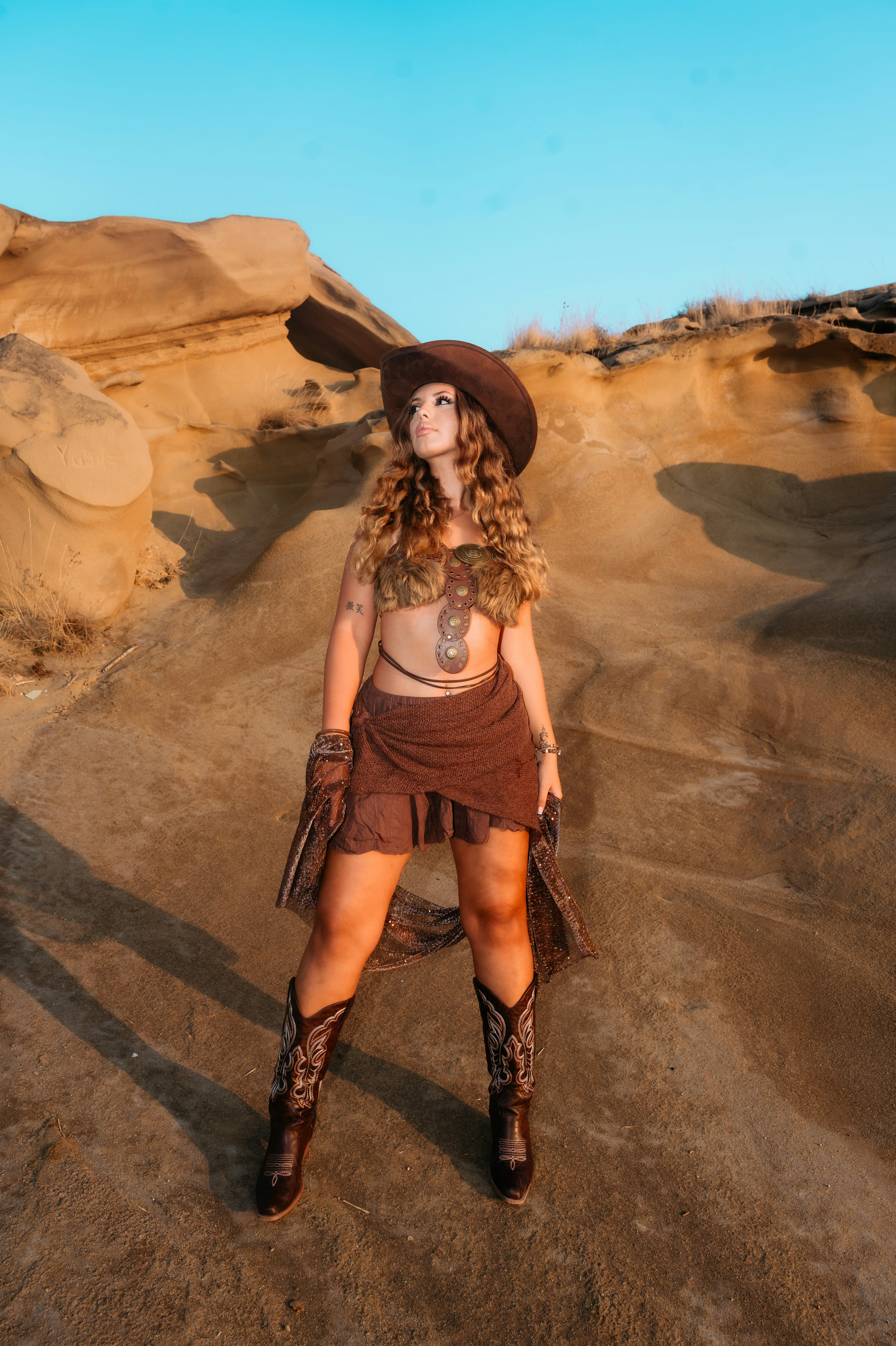 A woman in a brown hat and cowboy boots standing in a rocky desert
