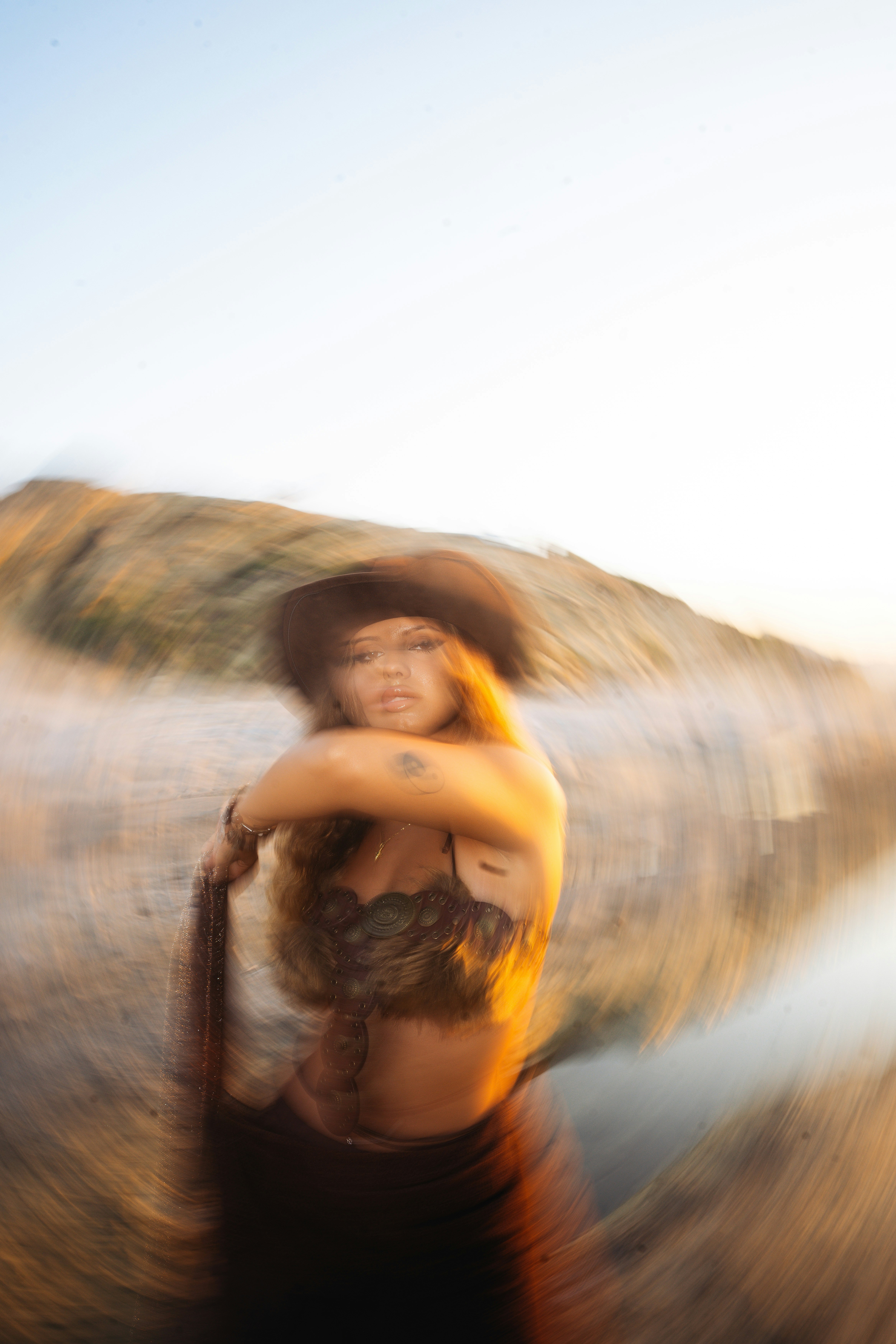A woman in a brown hat and fur top against a blurred coastal landscape