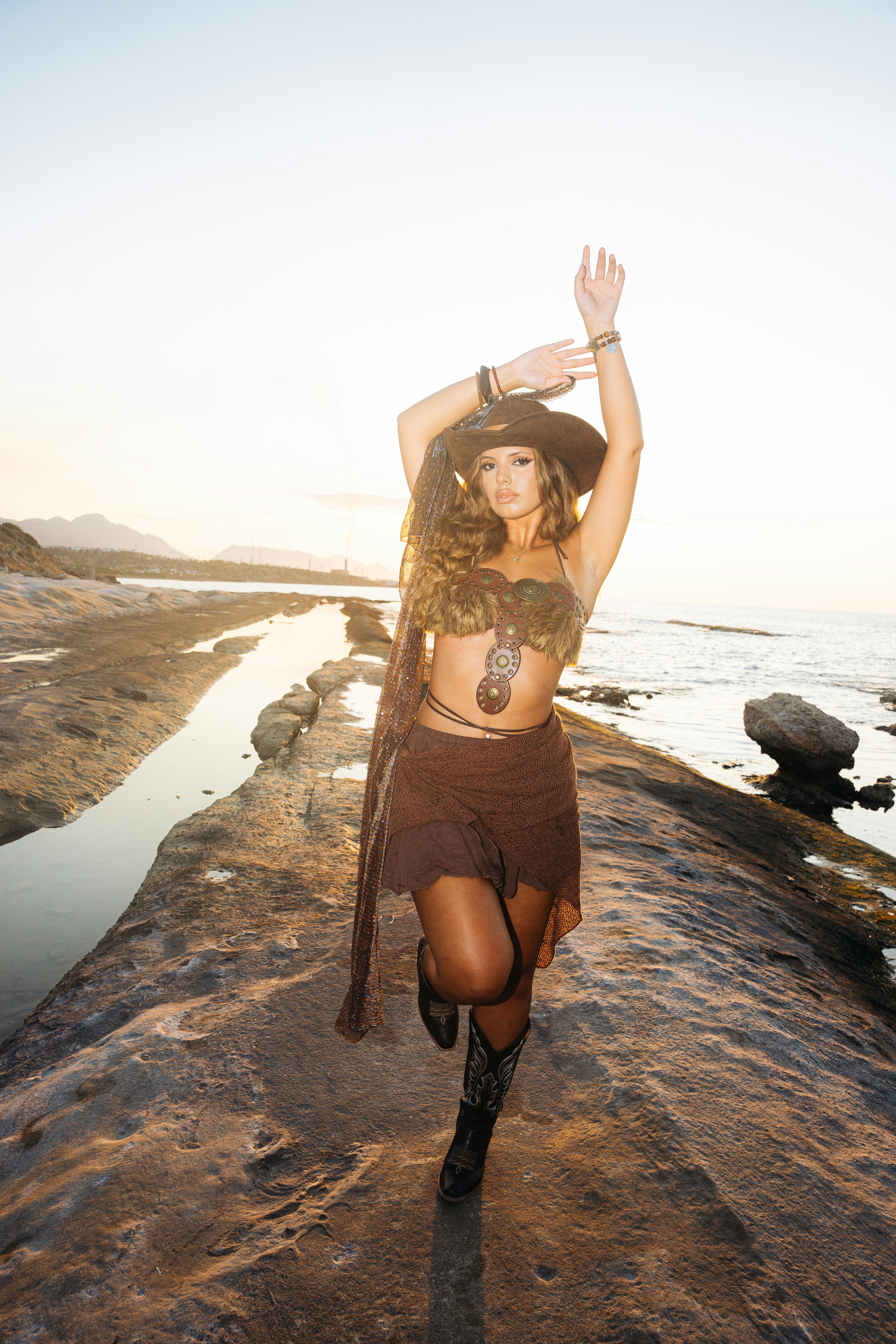 A woman in a cowboy hat and boots posing on a rocky coastal shelf