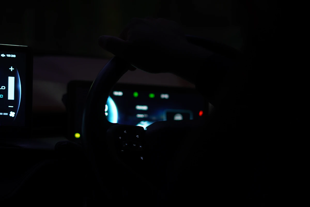 A person holding a steering wheel in a dark car interior with glowing displays