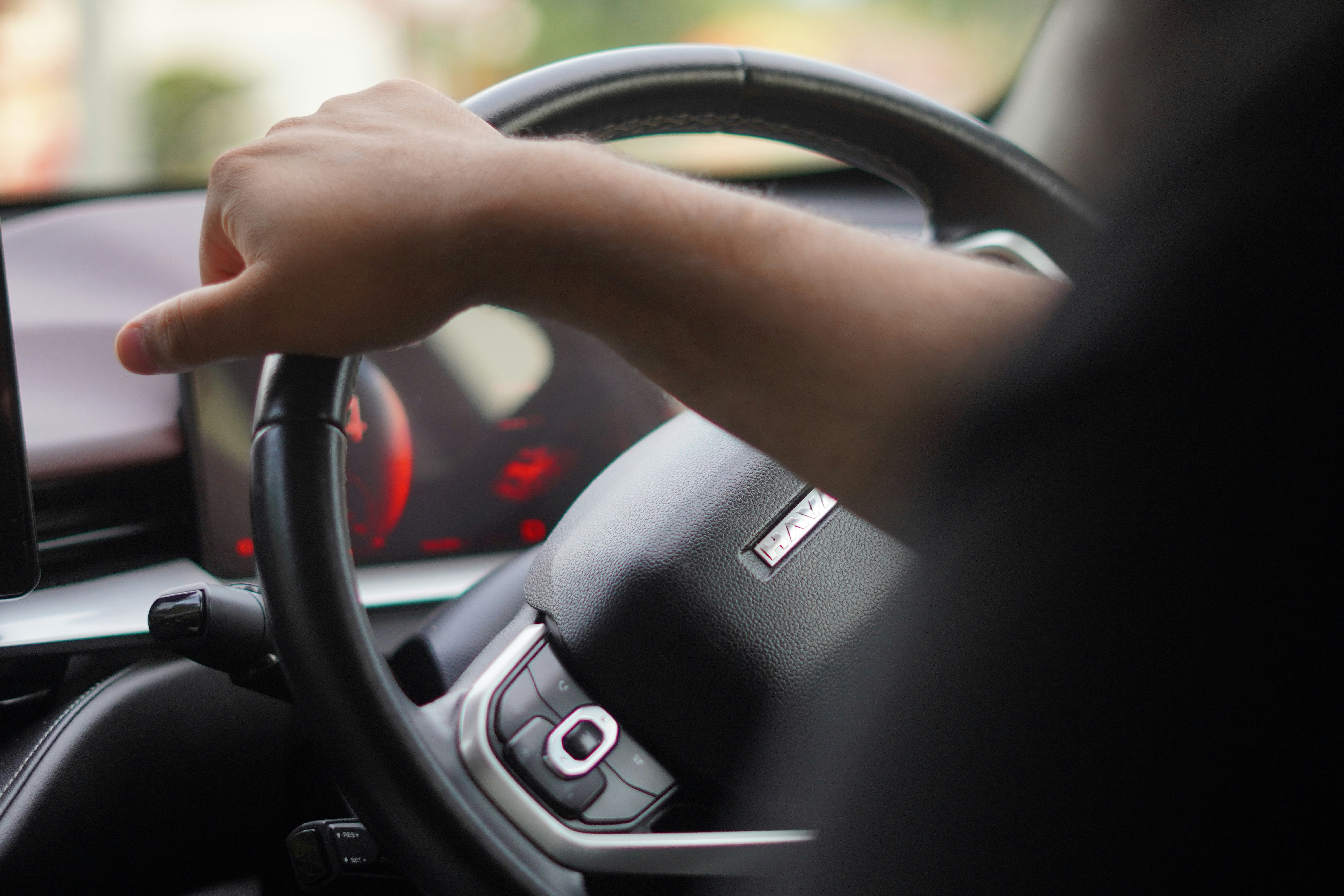 Close-up of a driver's arm resting on a leather steering wheel next to a modern digital touchscreen displaying climate controls.