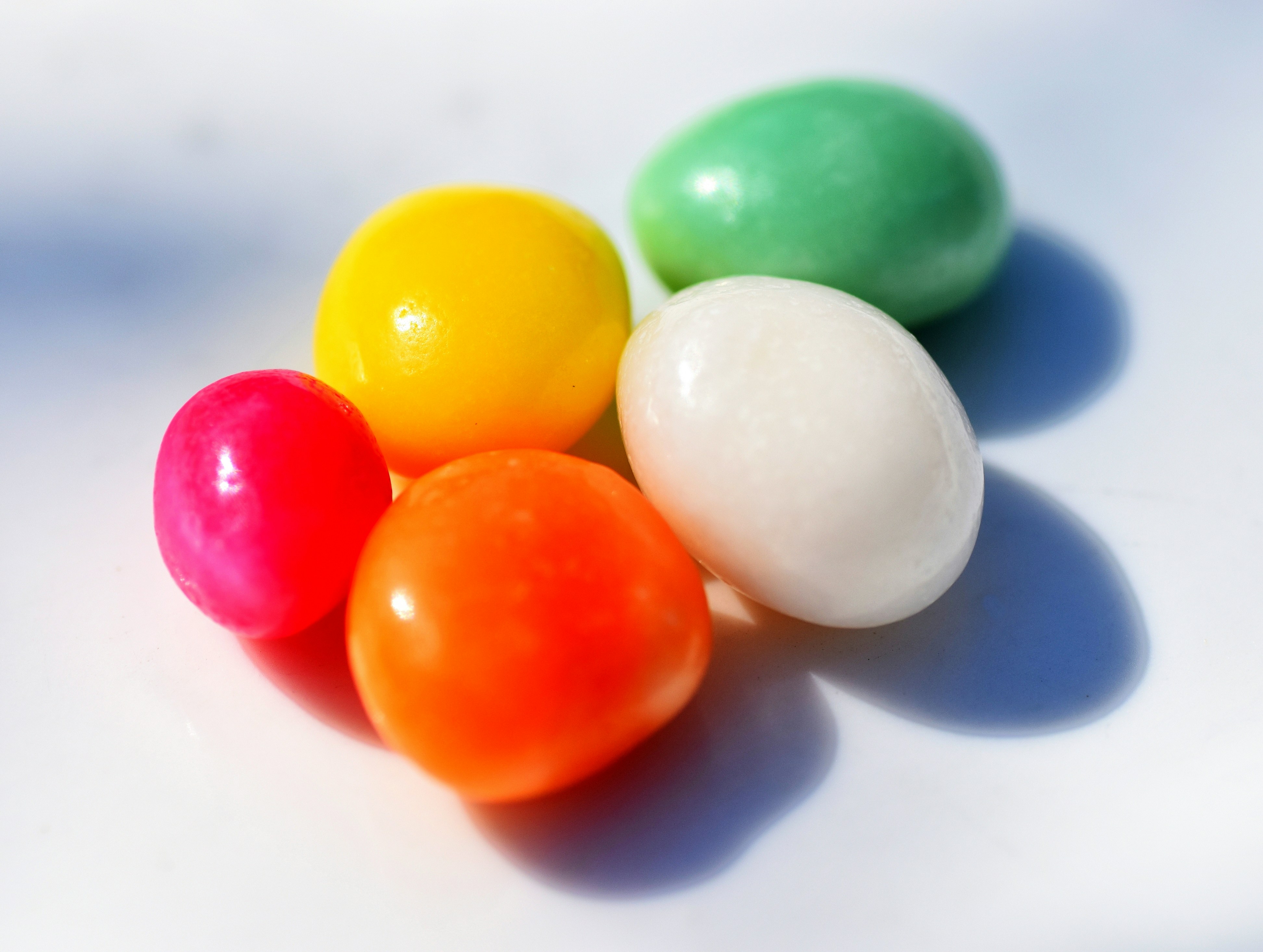 Five colorful round candies on a white surface with distinct shadows