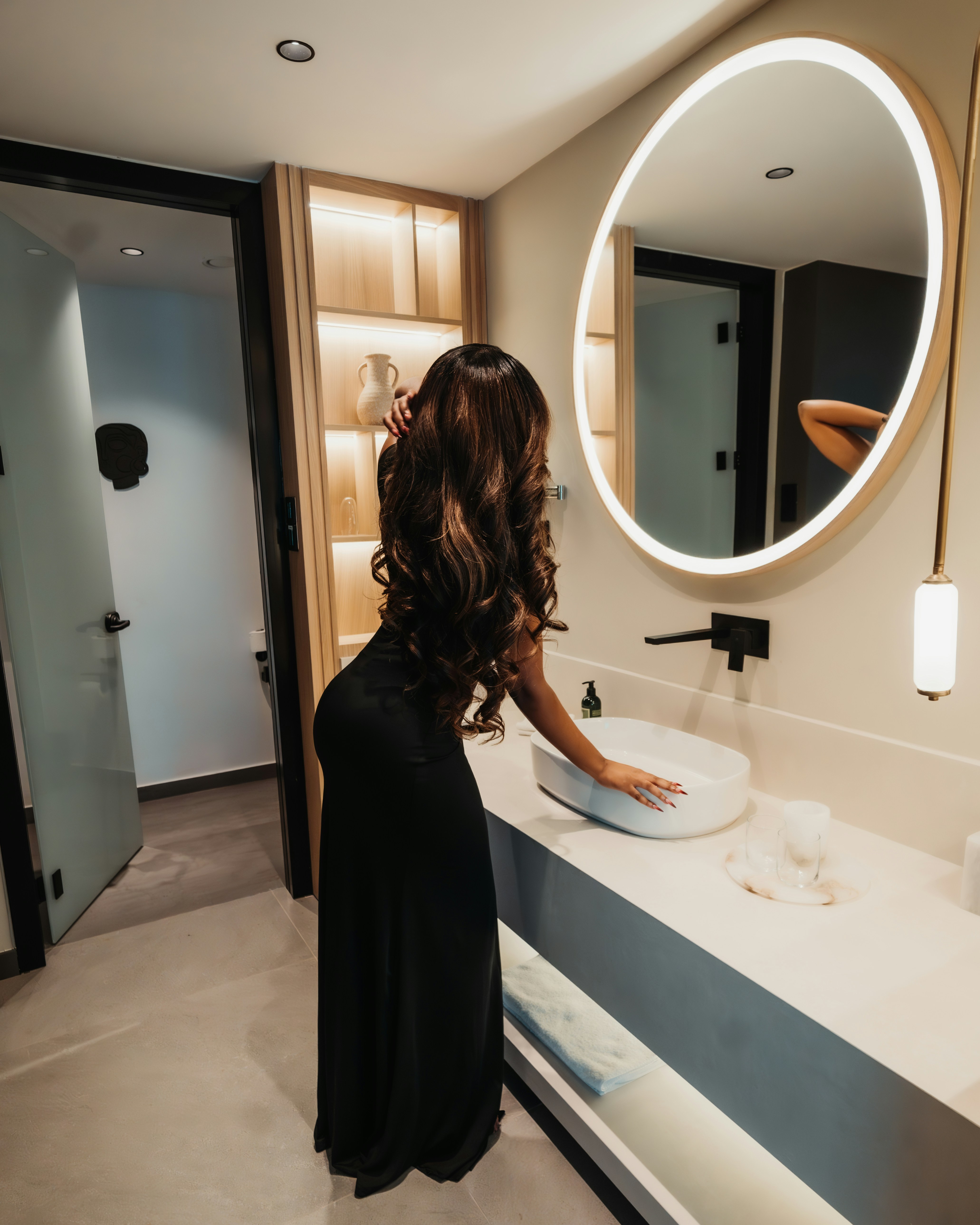 A woman with long dark hair in a black dress touching a bathroom sink