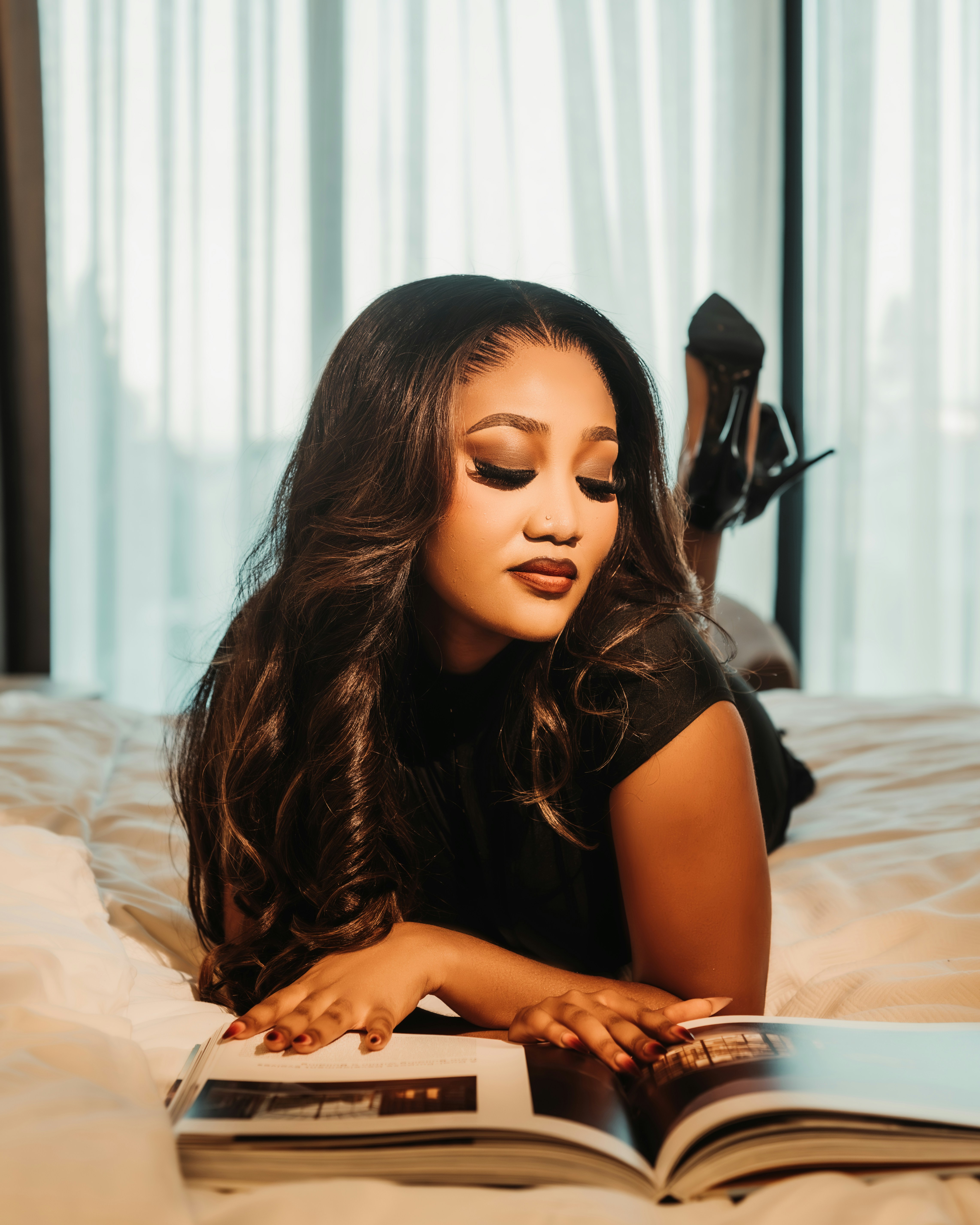 A woman with long dark hair reading a book on a white bed