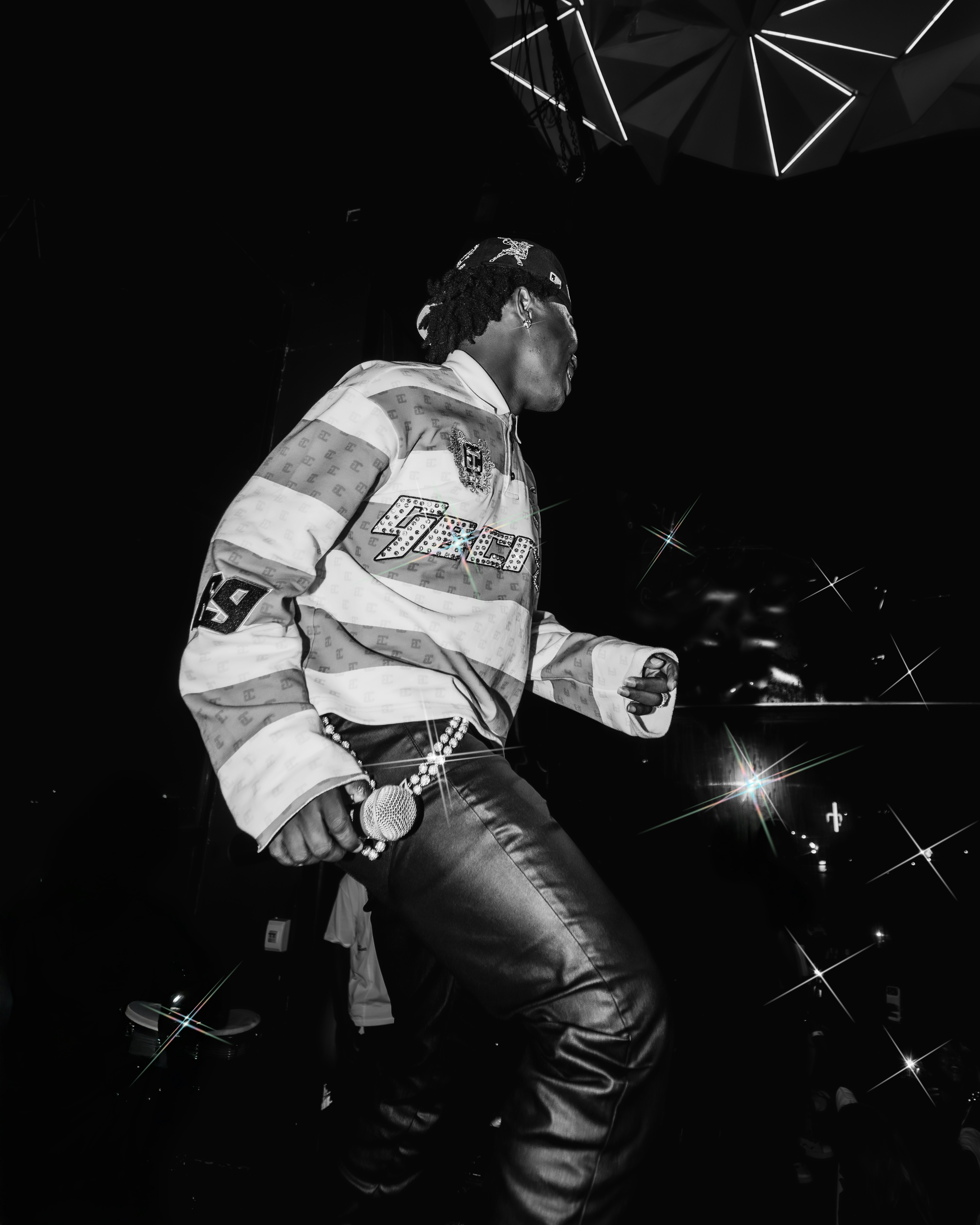 A person in a patterned long-sleeve shirt and leather pants holding a microphone