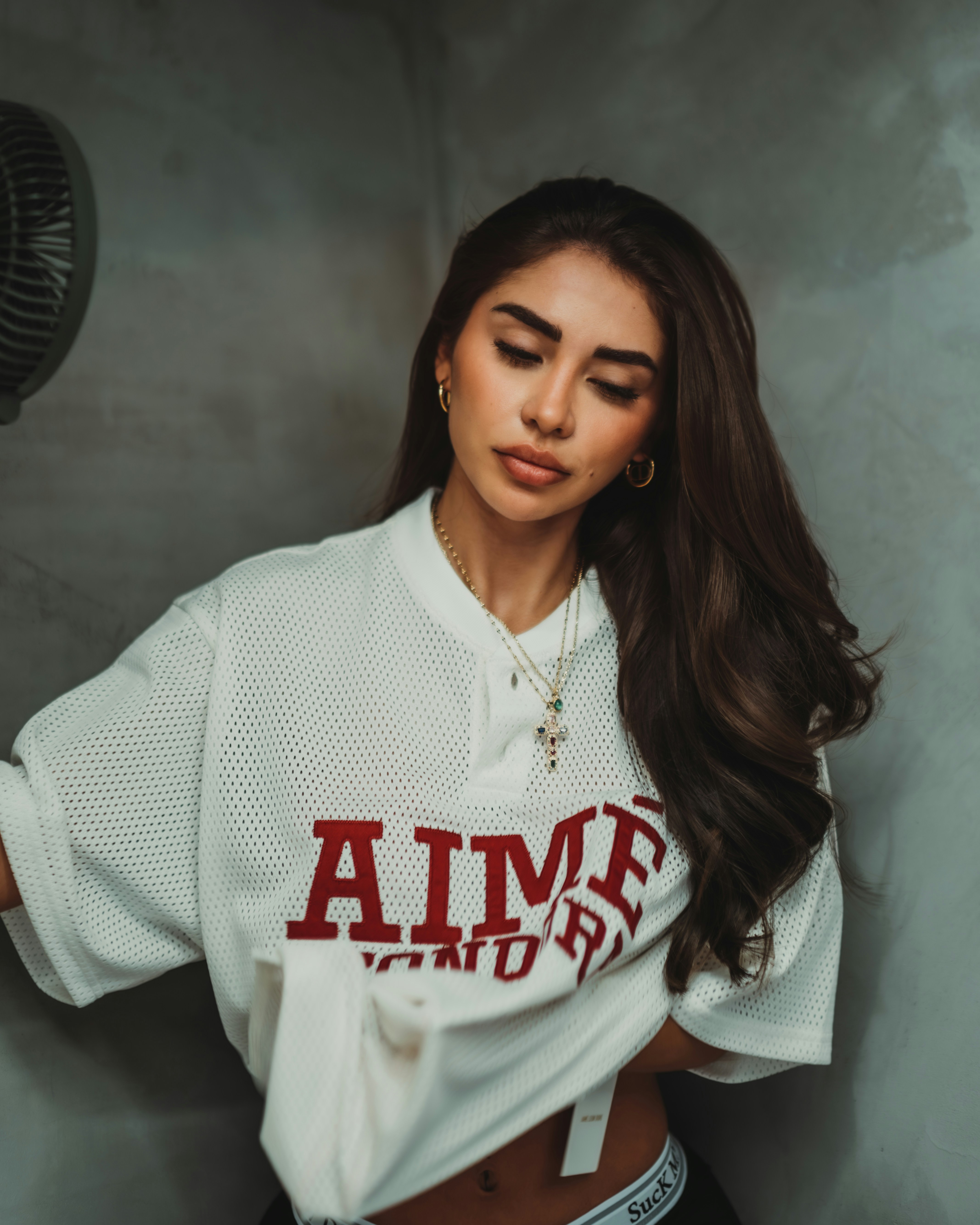 A woman with long dark hair wearing a white mesh shirt with red lettering