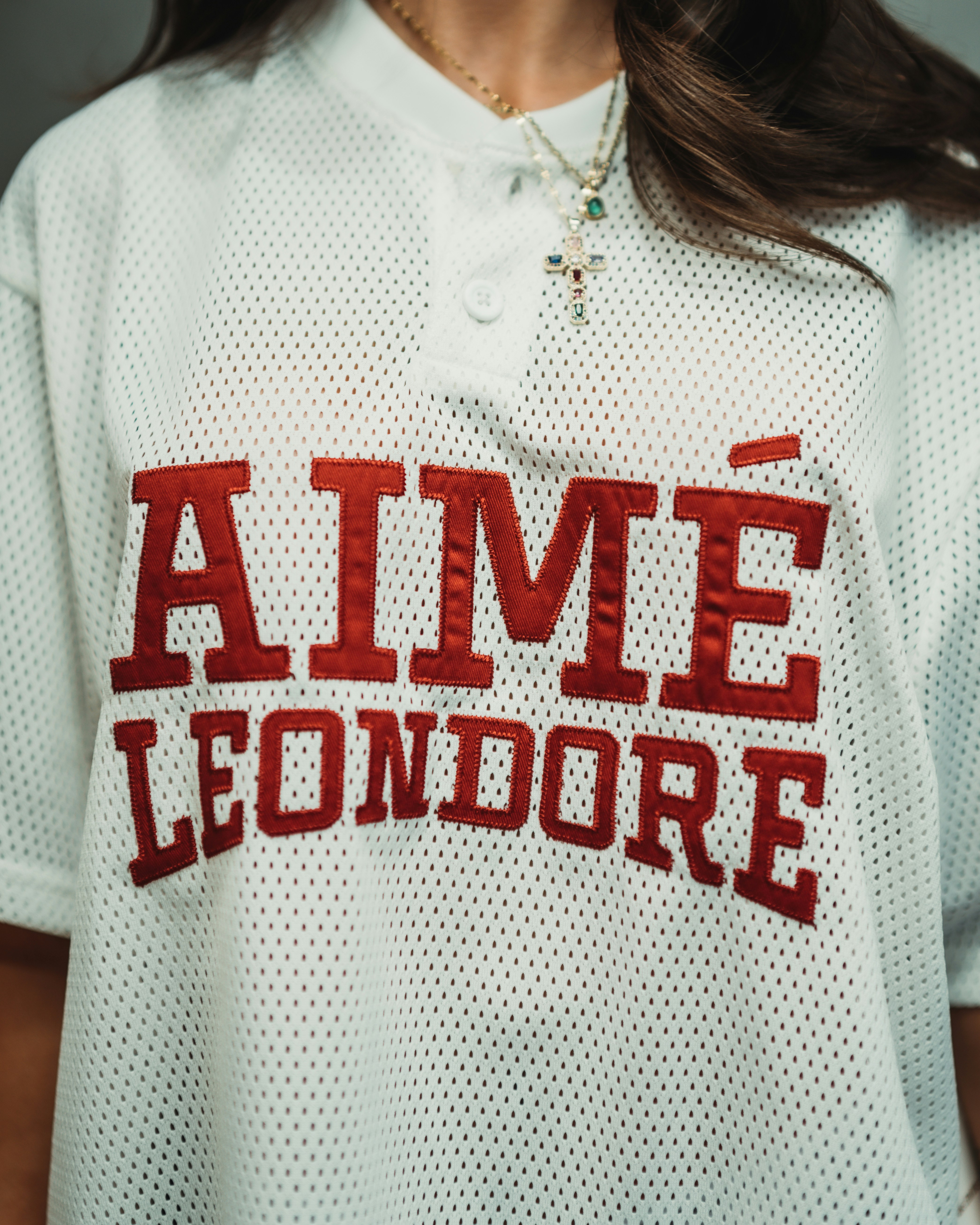 A person wearing a white mesh shirt with red lettering and a cross necklace