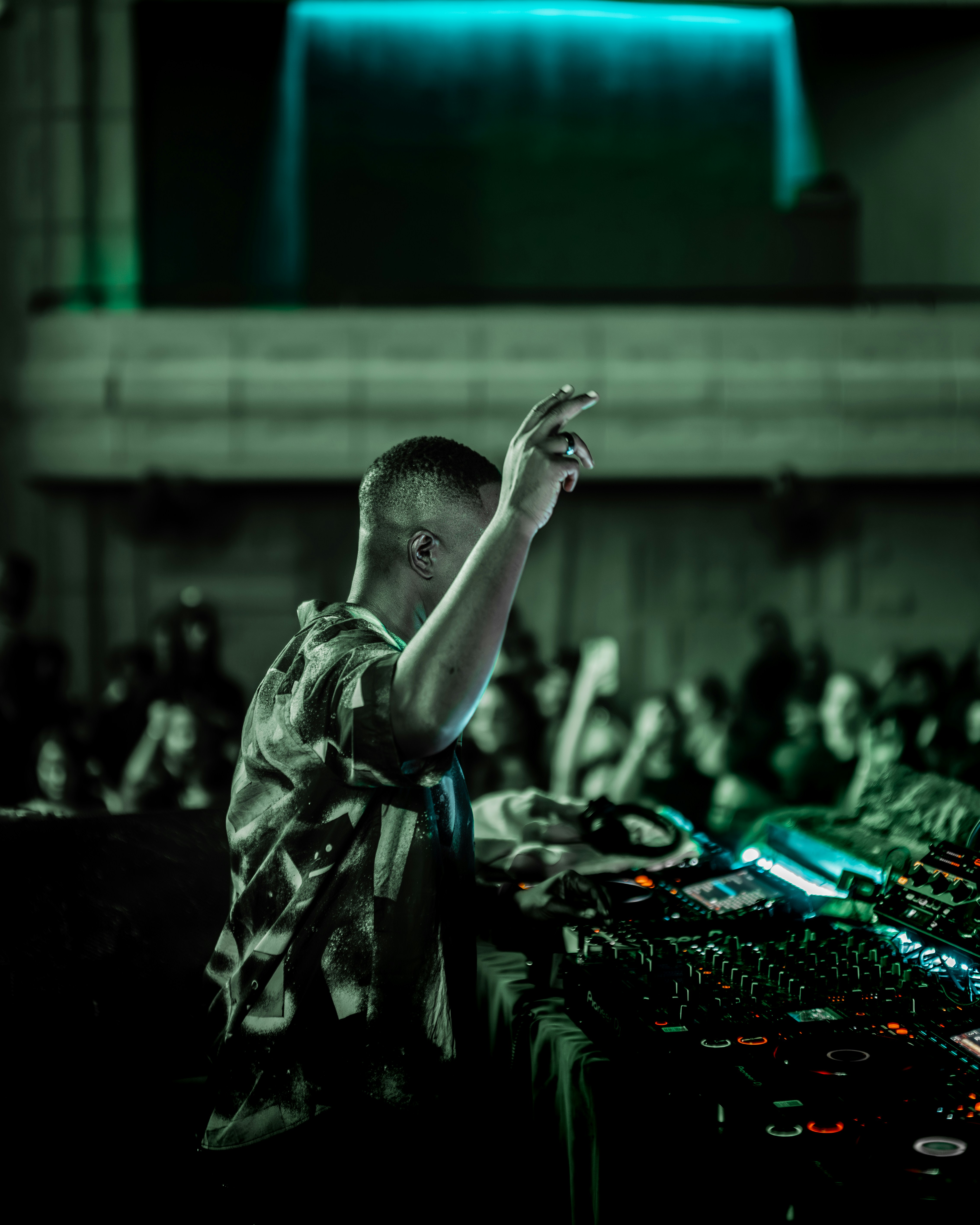 暗いクラブのミキシングコンソールに片腕を上げたDJ
