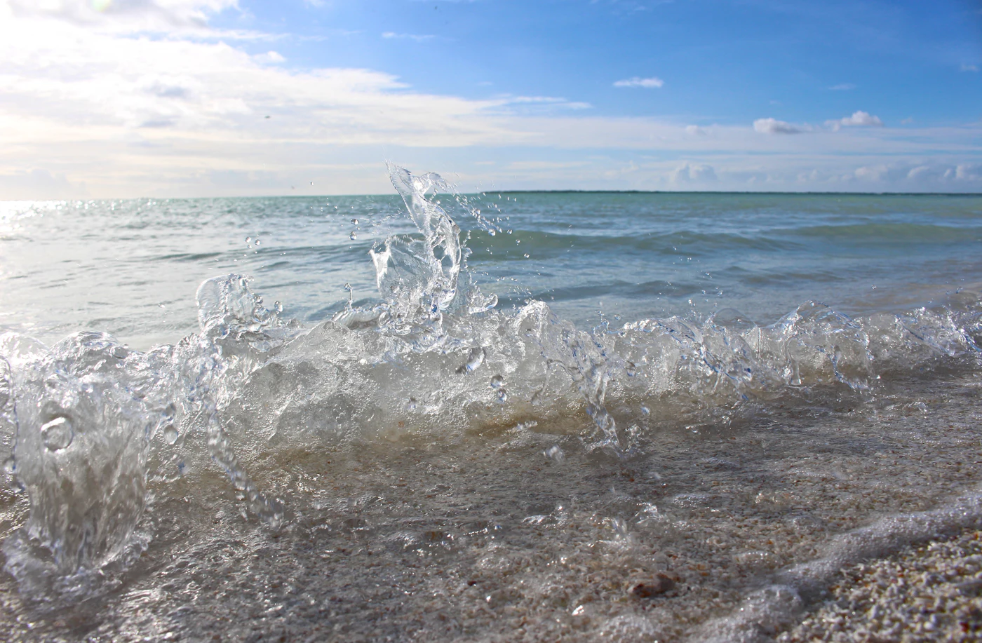 A small wave breaking on a sandy beach under a bright blue sky