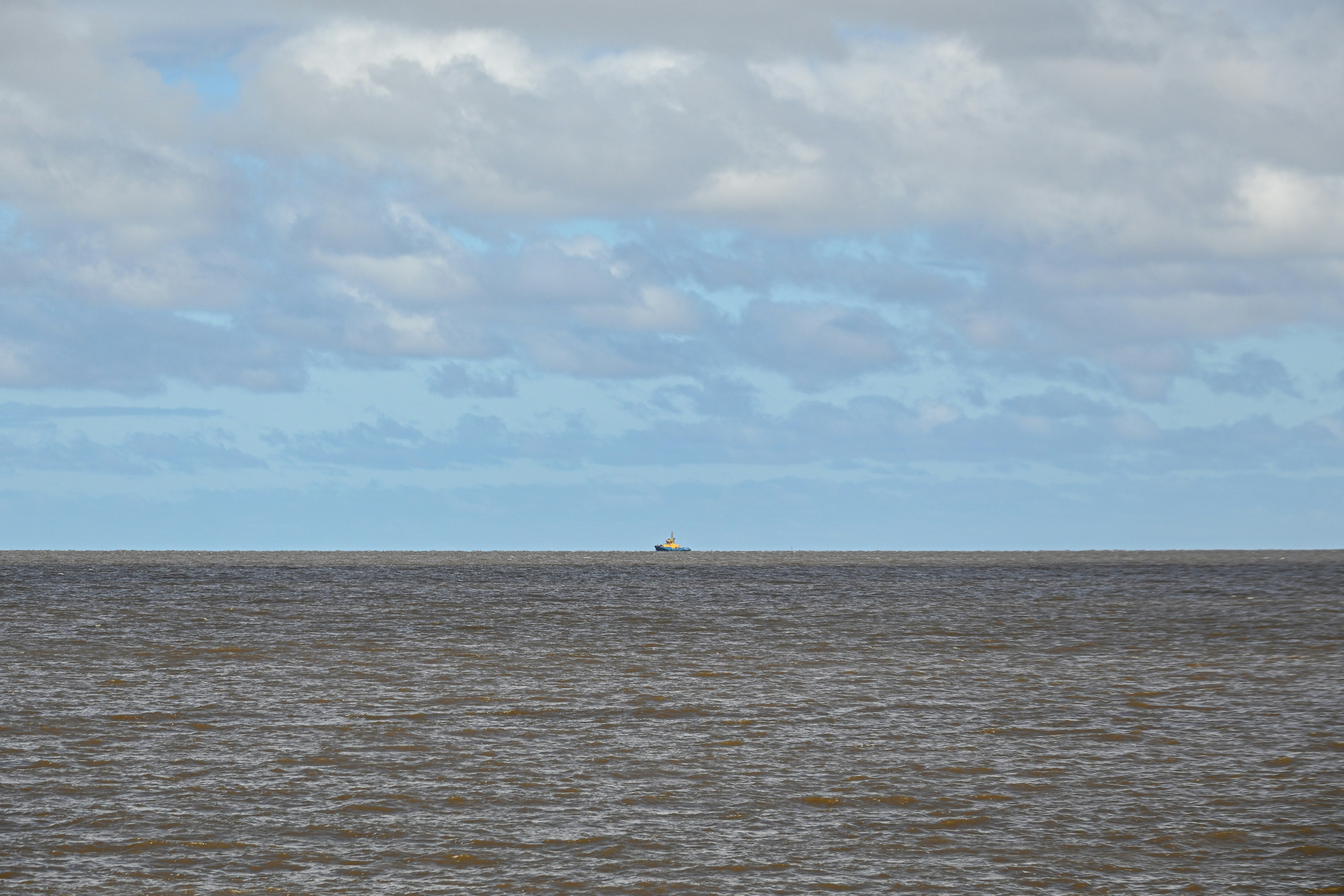 Un petit remorqueur à l’horizon d’une vaste mer sombre sous un ciel nuageux