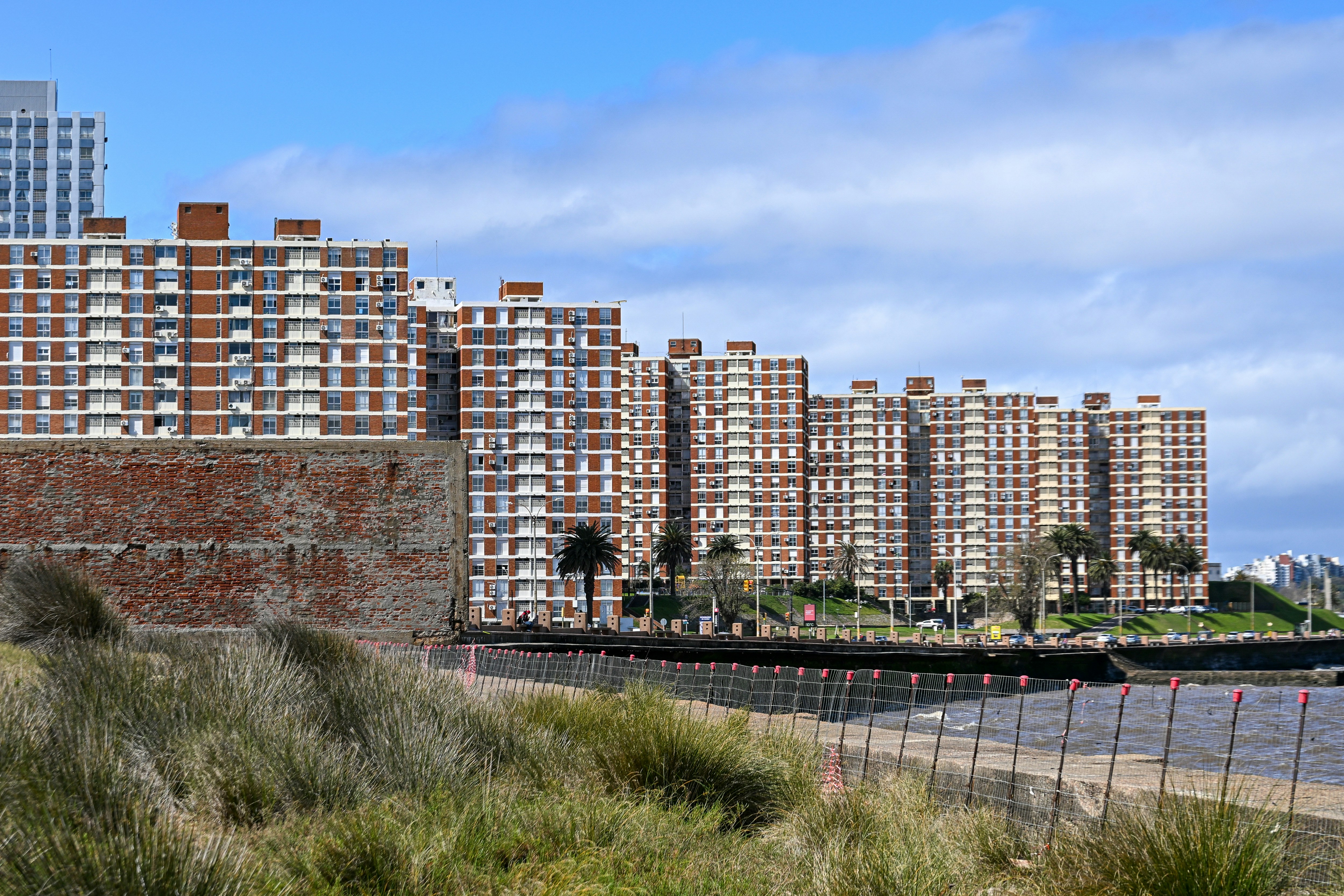 De hauts immeubles en briques derrière un mur de briques usé et des dunes côtières herbeuses