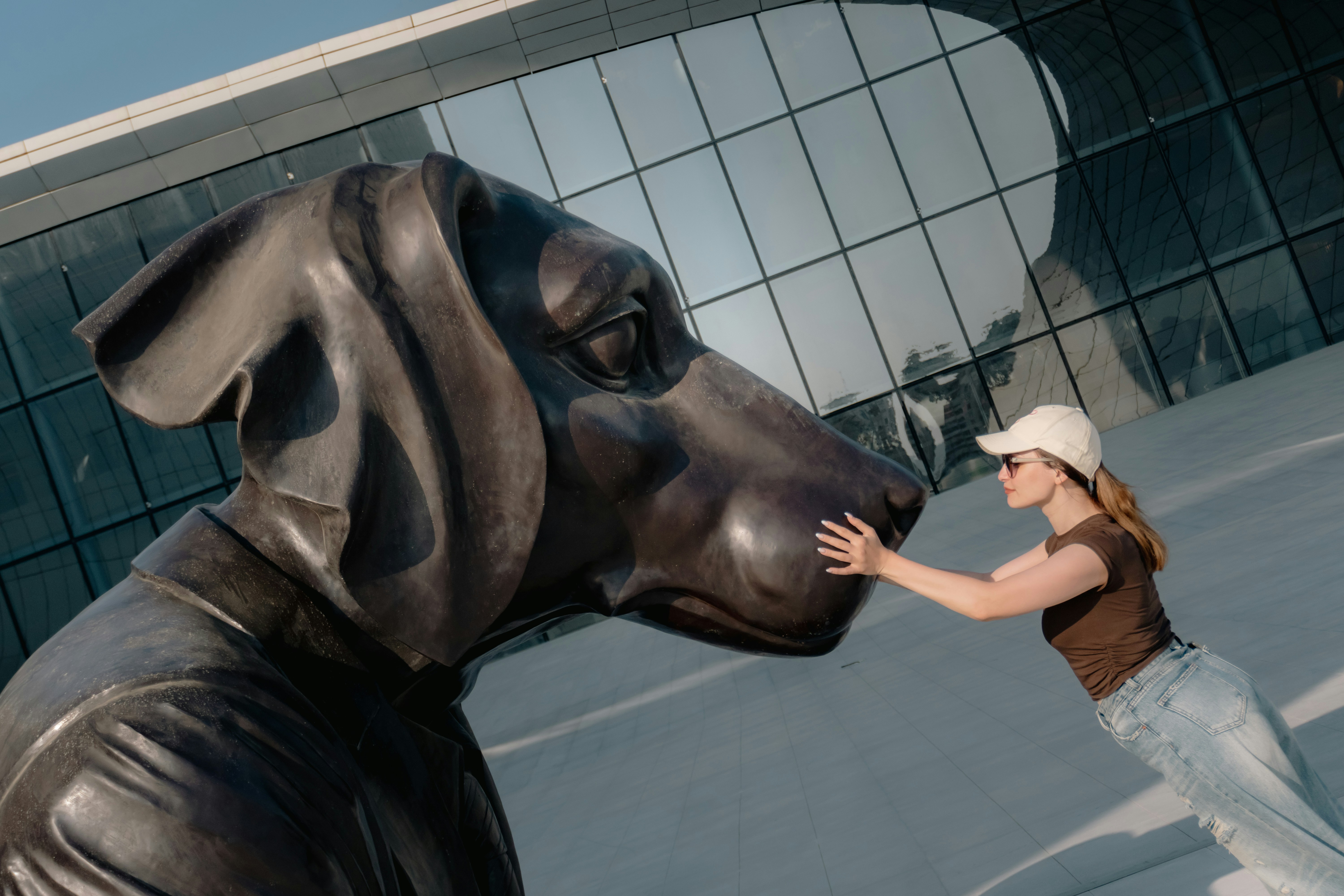 A woman in a cap touching the nose of a large bronze dog sculpture