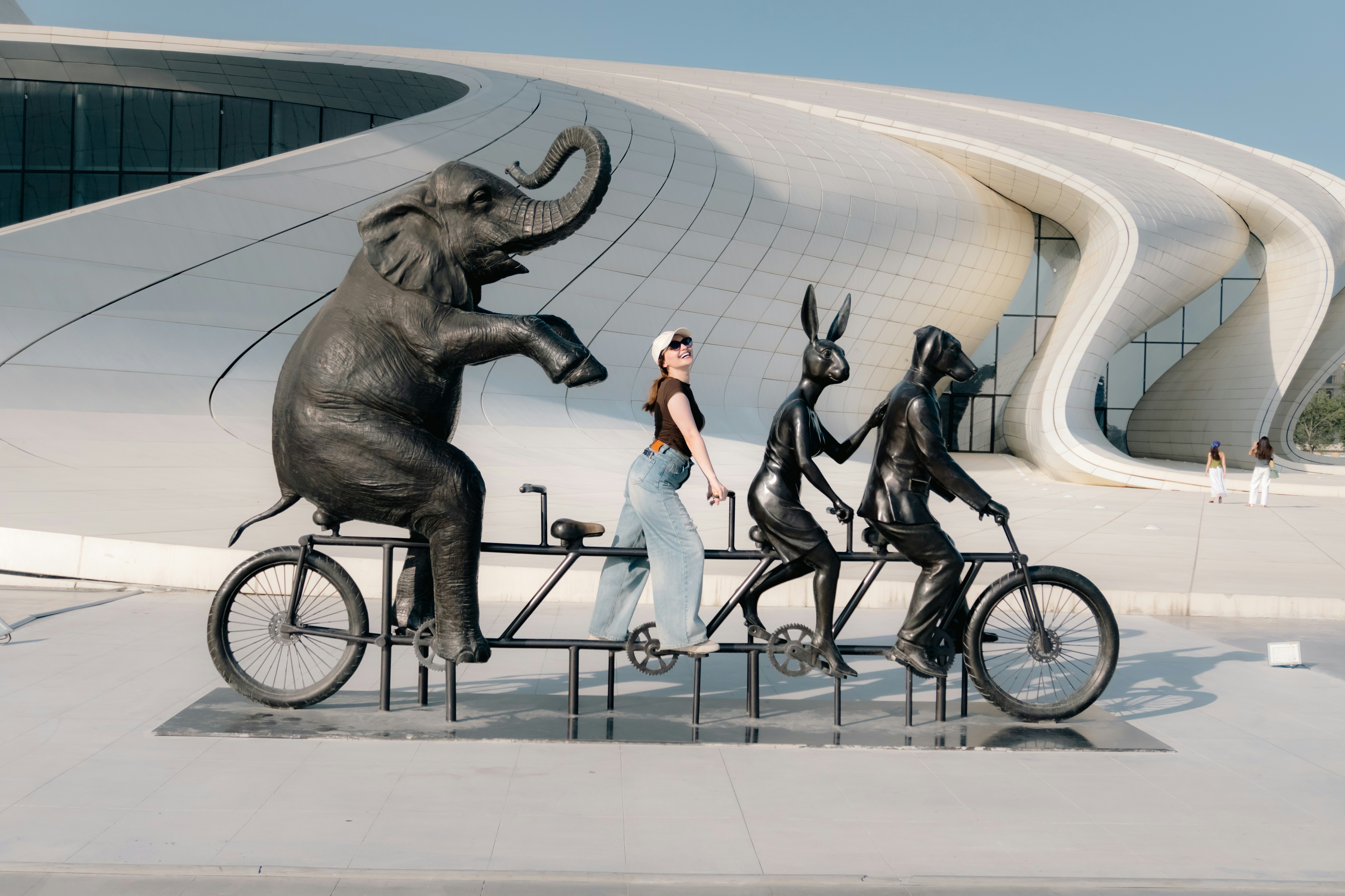 A woman posing on a tandem bicycle with bronze elephant, rabbit, and dog statues