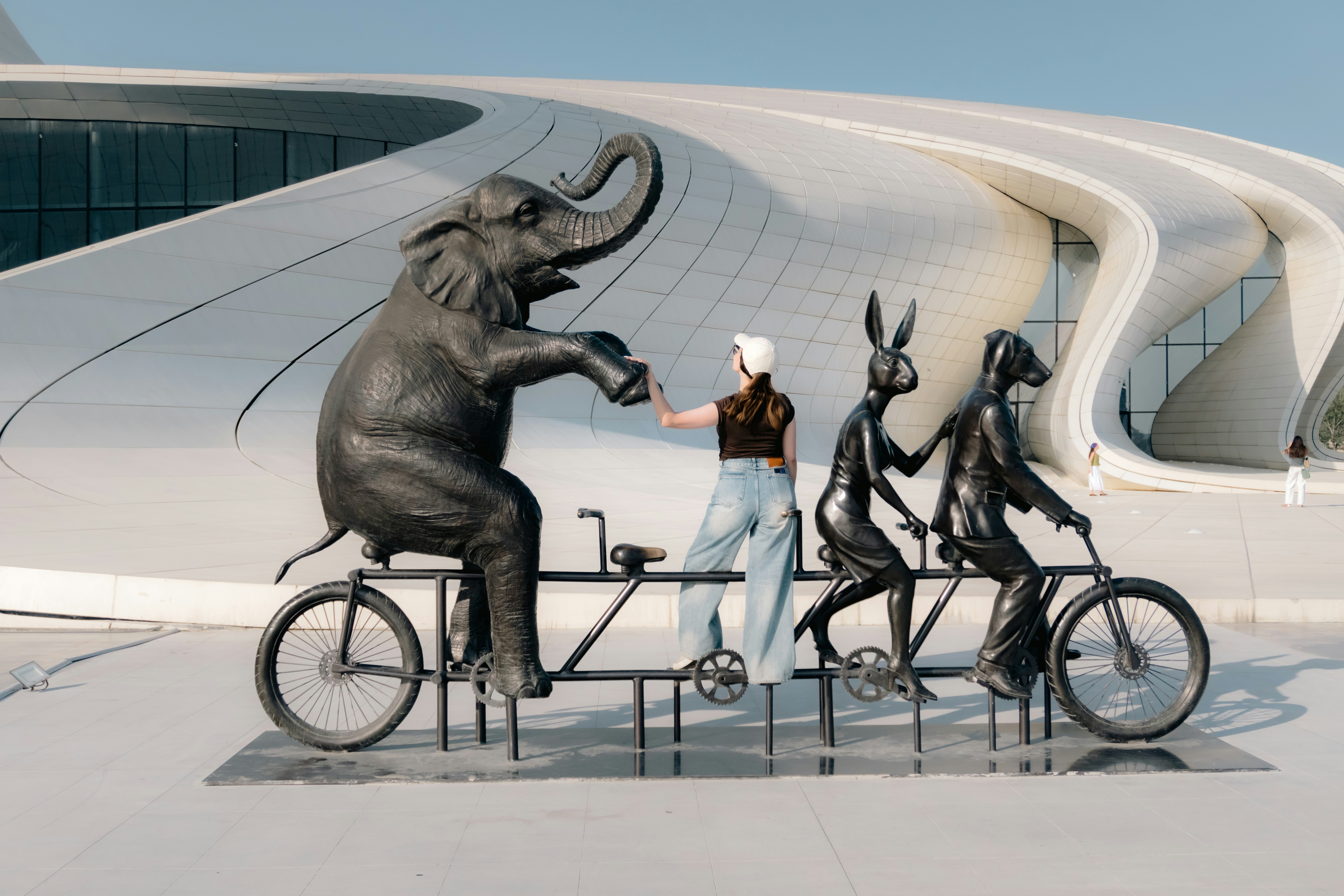 A woman standing on a tandem bicycle with elephant, hare, and dog statues