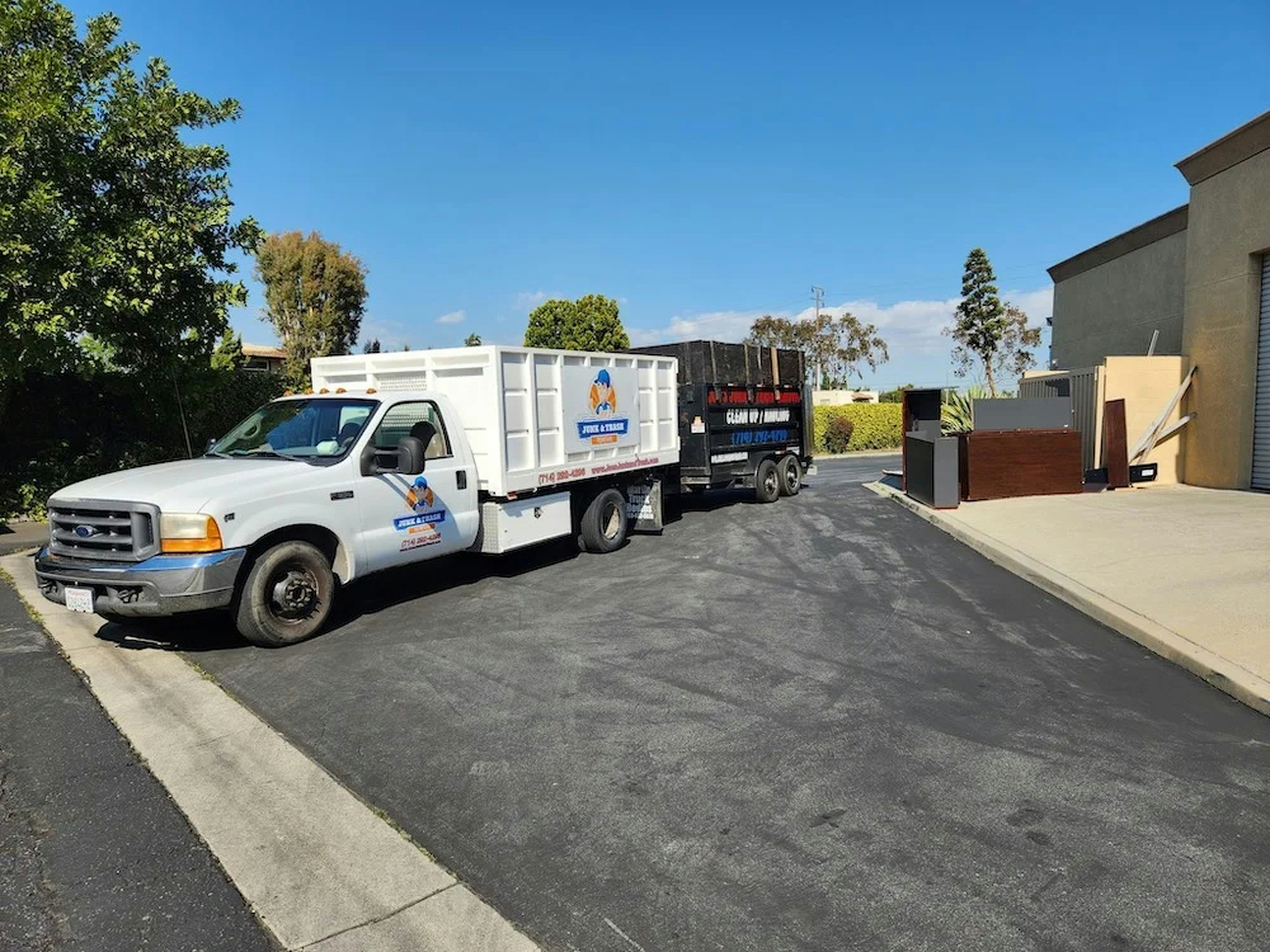 A white pickup towing a black dump trailer across a paved lot