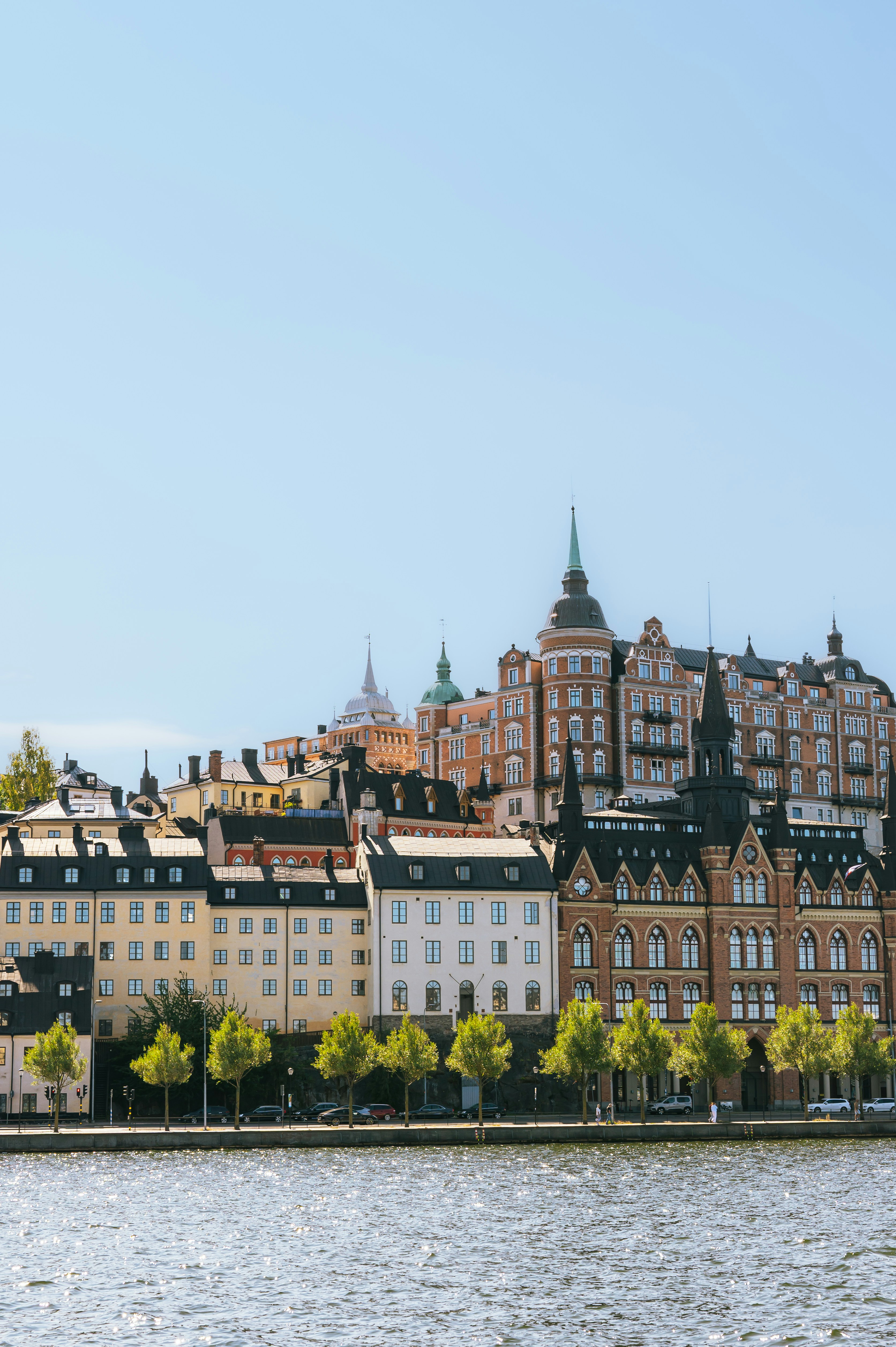 Historic buildings along a waterfront in Stockholm with a row of green trees