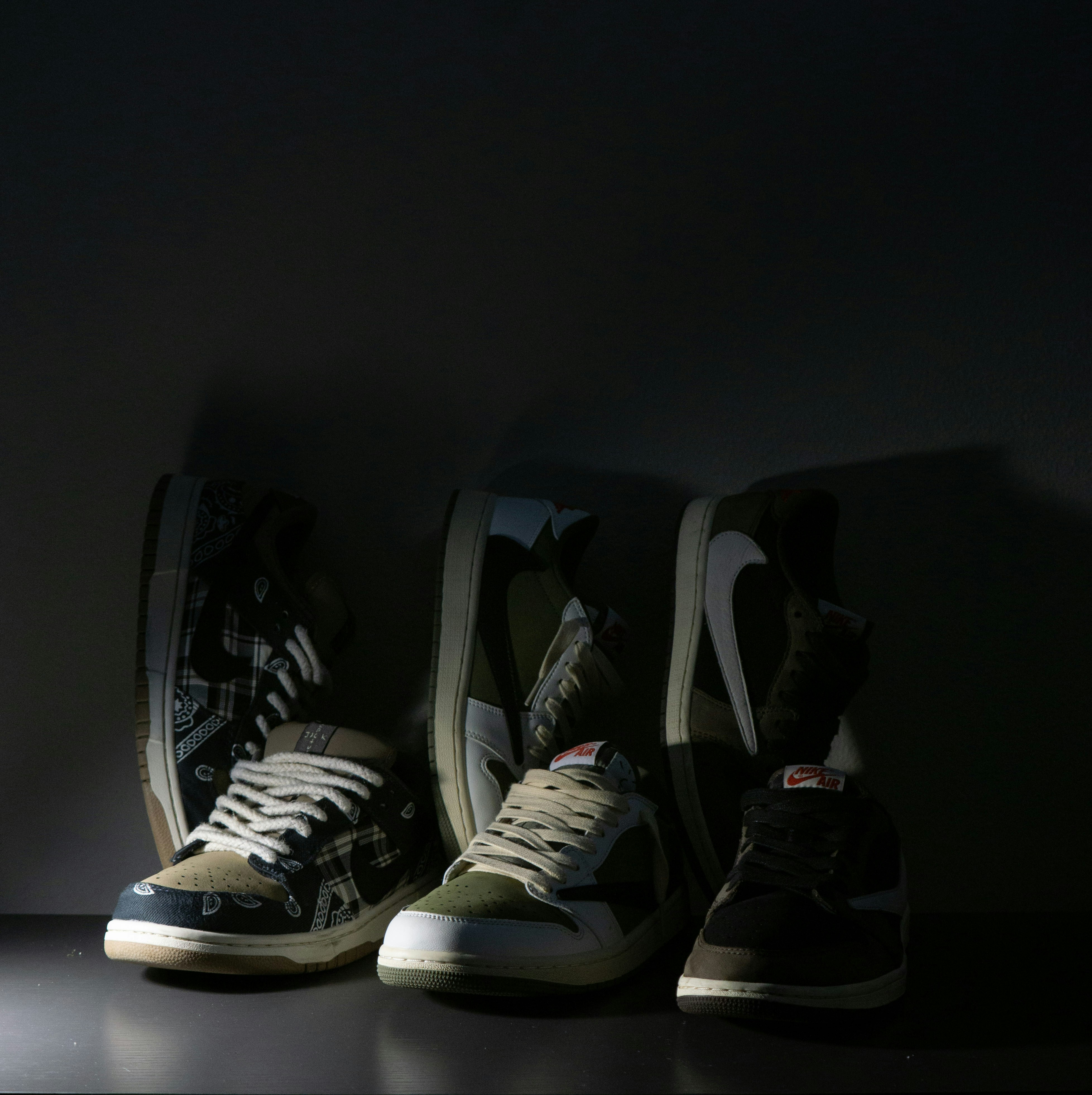 Three pairs of low-top sneakers arranged on a dark surface in dim light