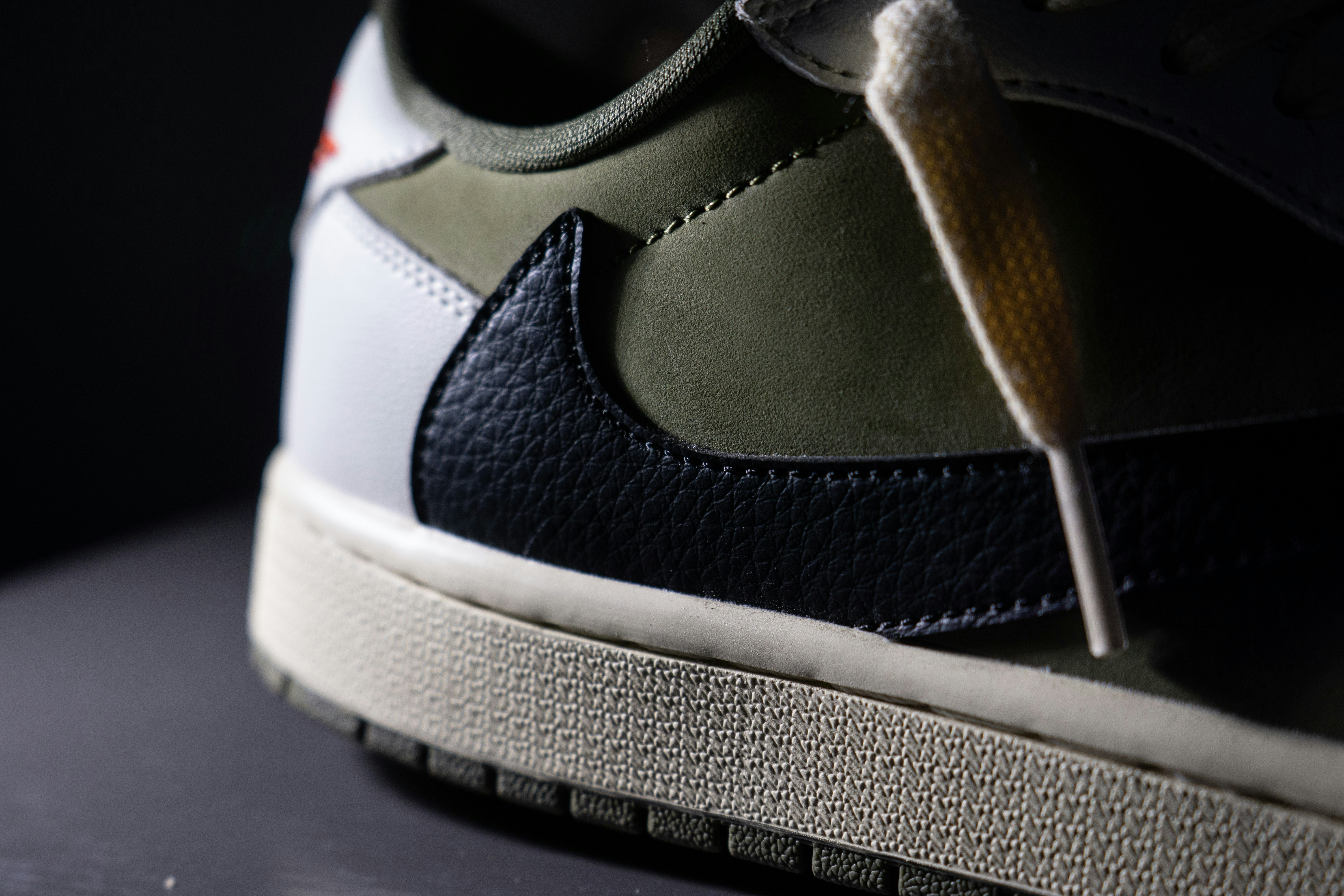 A close-up of an olive green and black leather sneaker with white accents