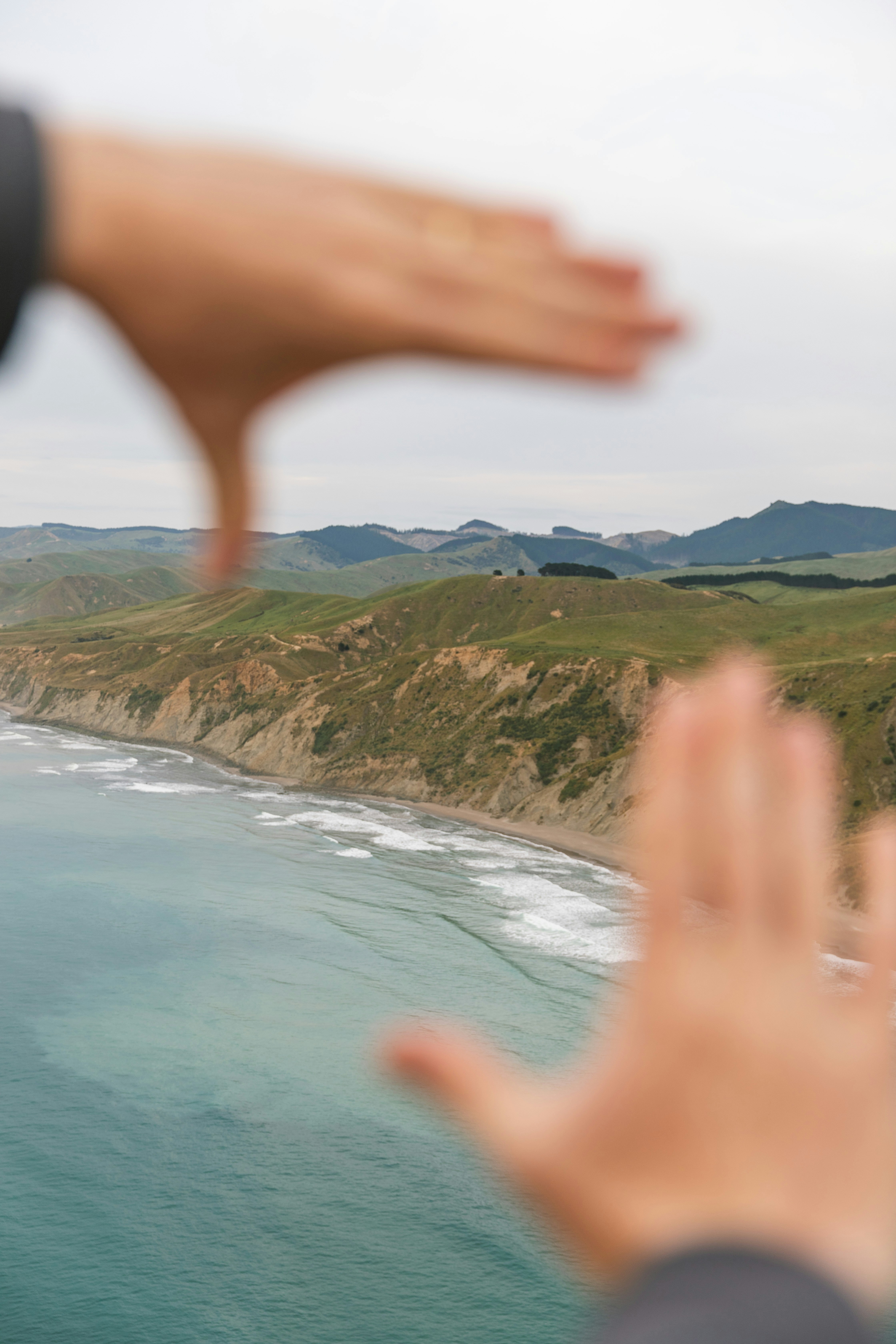 Hands framing a view of a green coastline with cliffs and ocean waves