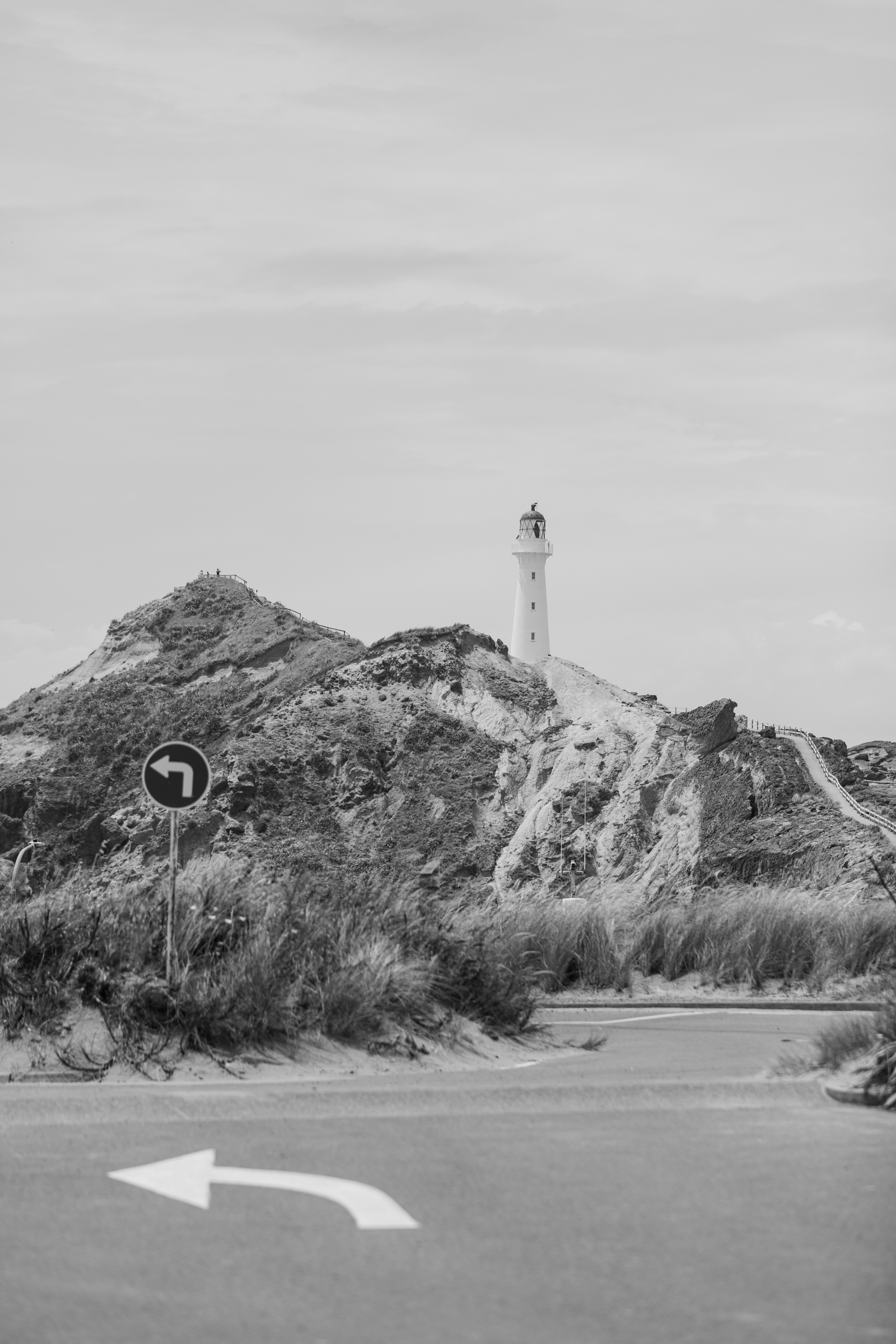 A white lighthouse on a rocky hill above a road with a turn sign