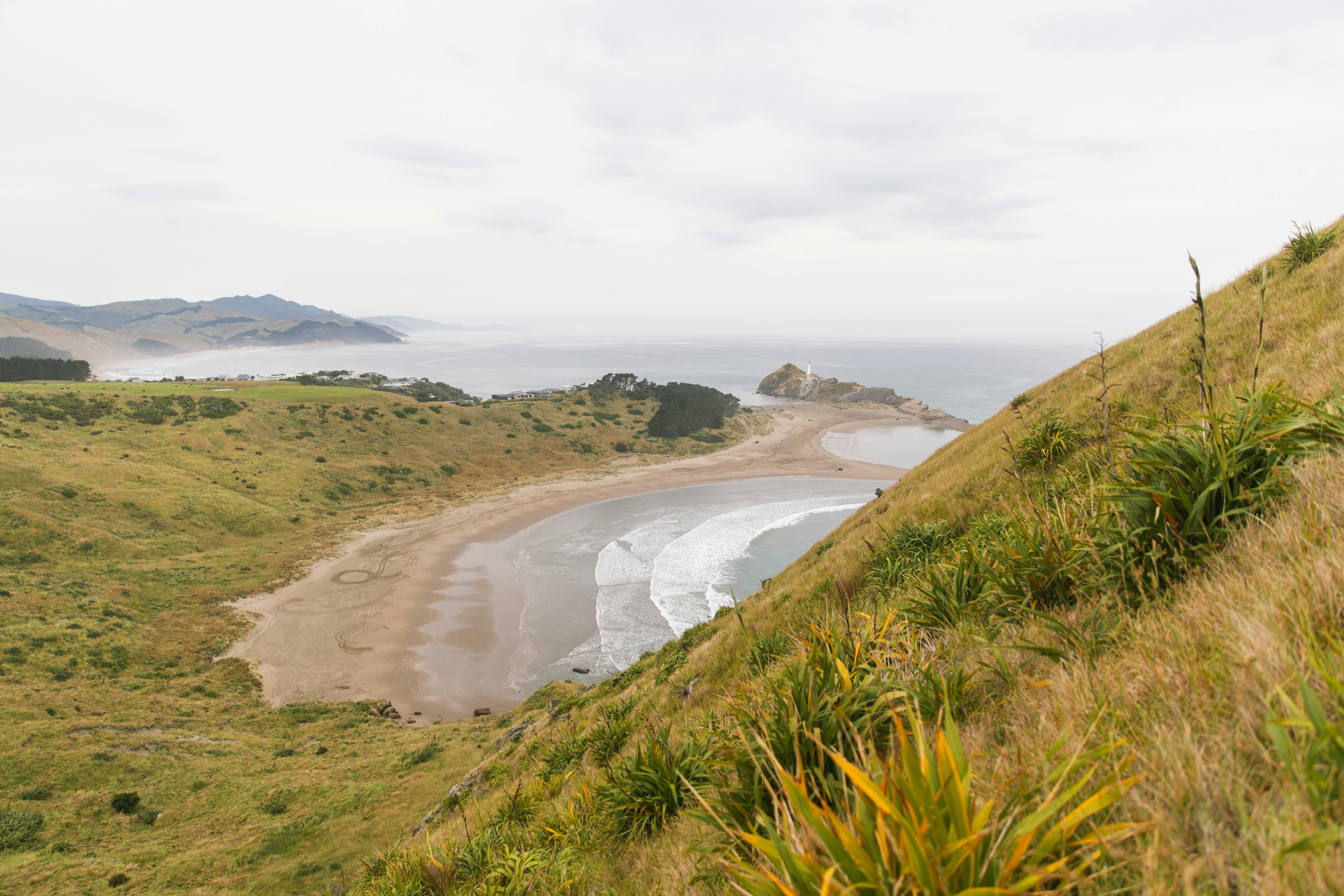 A sandy beach in a cove surrounded by grassy hills under a cloudy sky