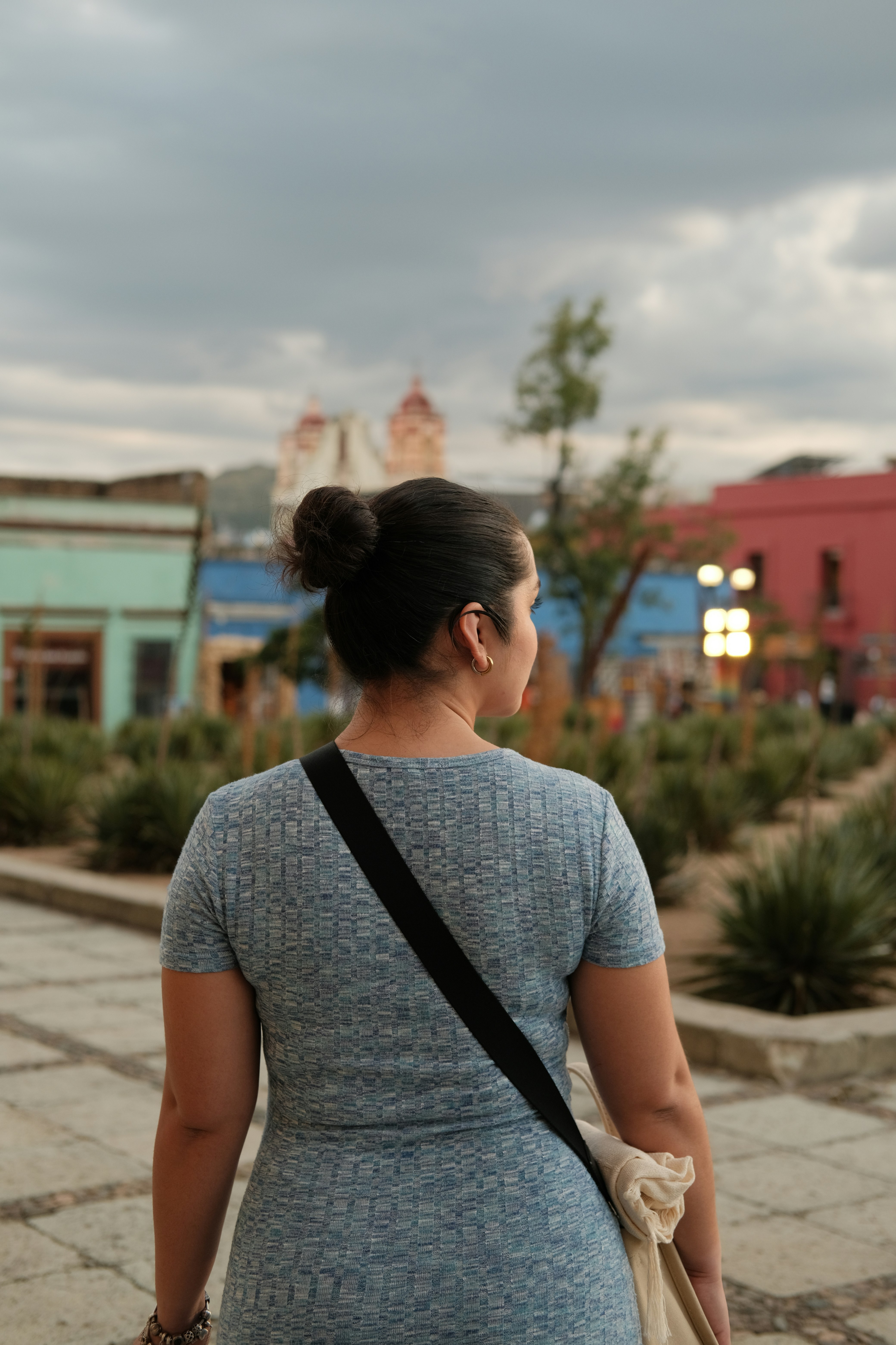 Una mujer con el pelo recogido en un moño vista desde atrás en una plaza del pueblo