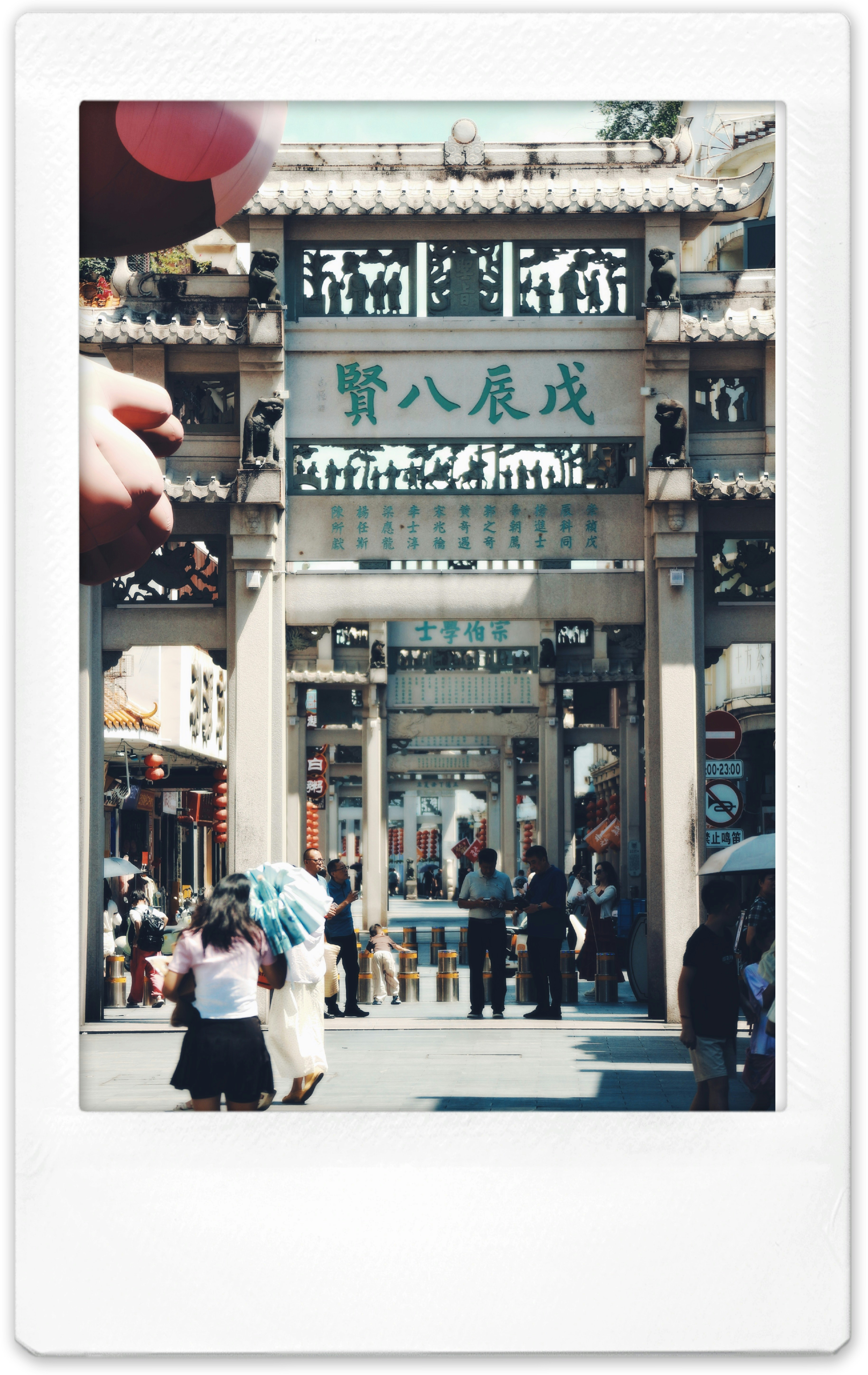 People walking through a stone archway with traditional Chinese carvings and calligraphy