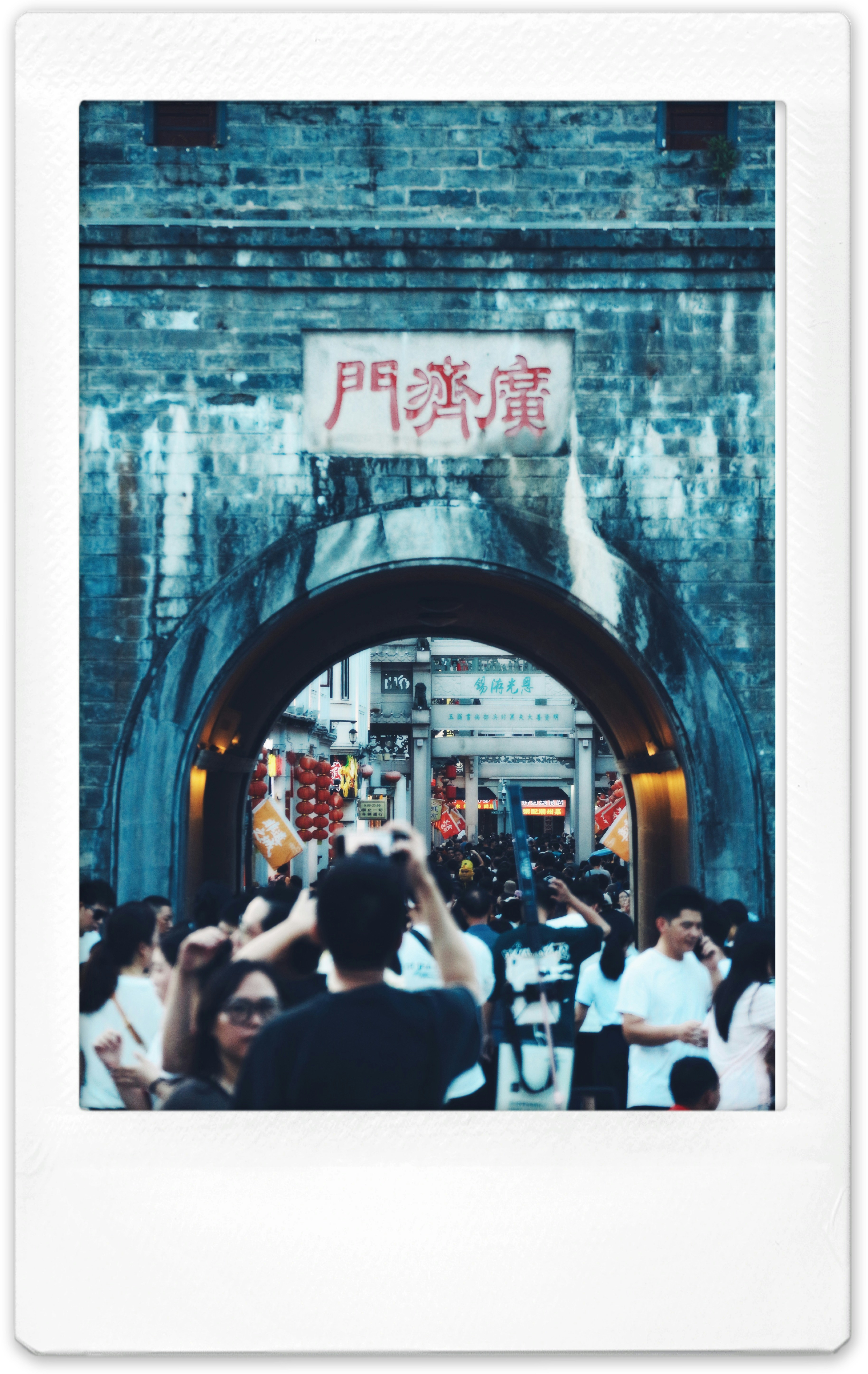 A crowd of people walking through a stone archway with red lanterns