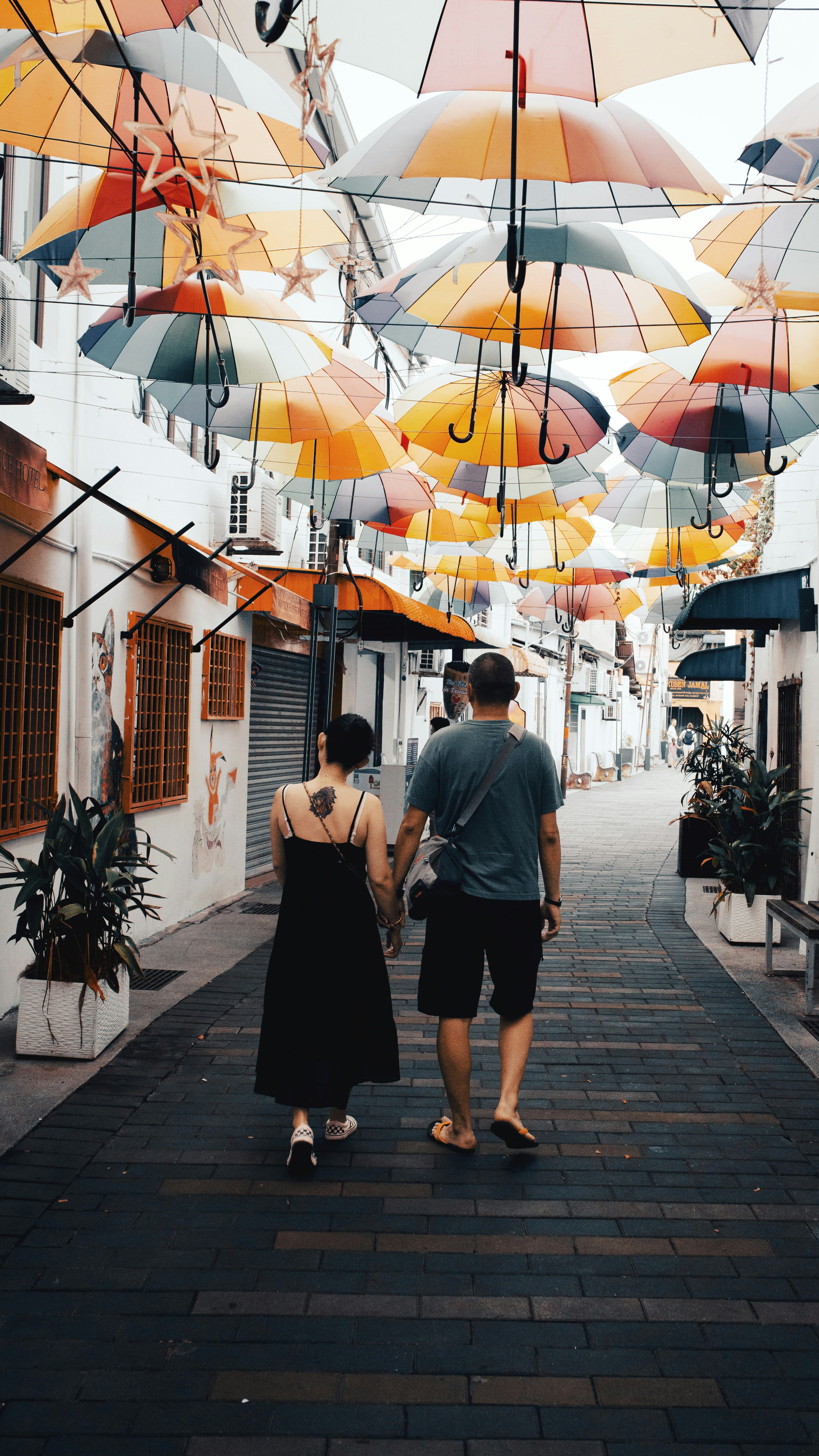 Un couple marchant main dans la main dans une ruelle étroite bordée de parapluies colorés suspendus
