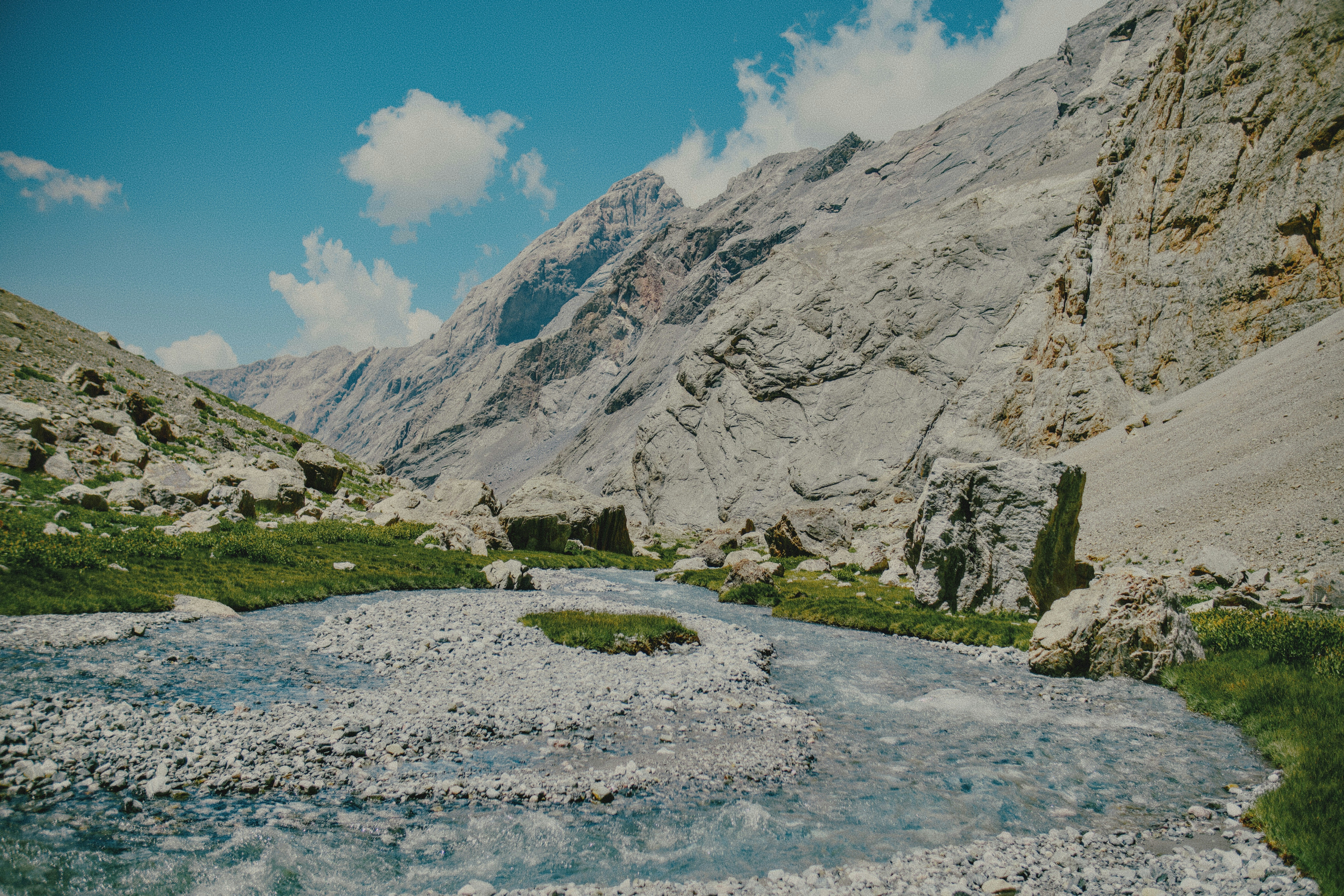 A shallow stream flowing through a rocky mountain valley under a blue sky