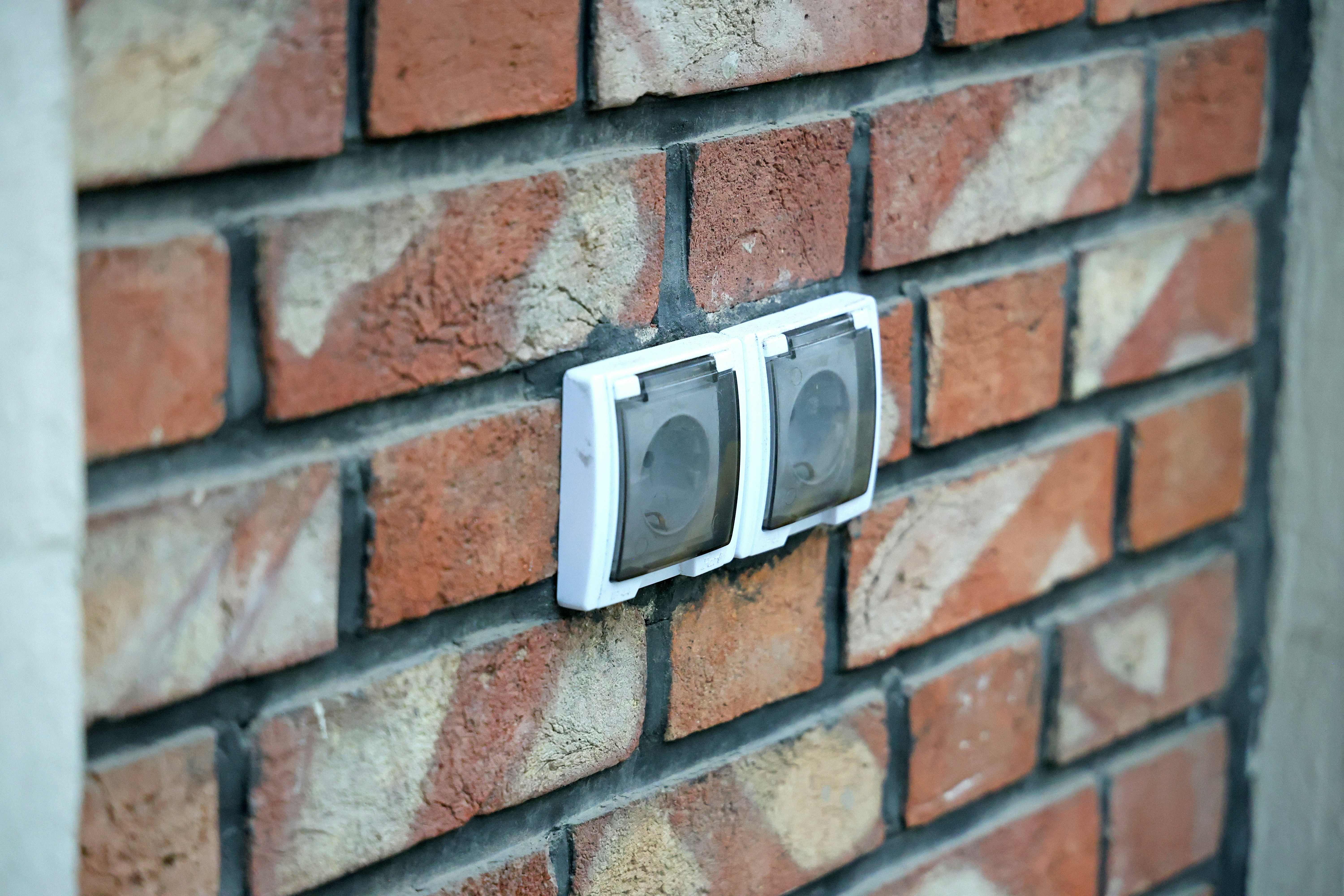 homeowner checking a weatherproof outdoor outlet cover on a house wall