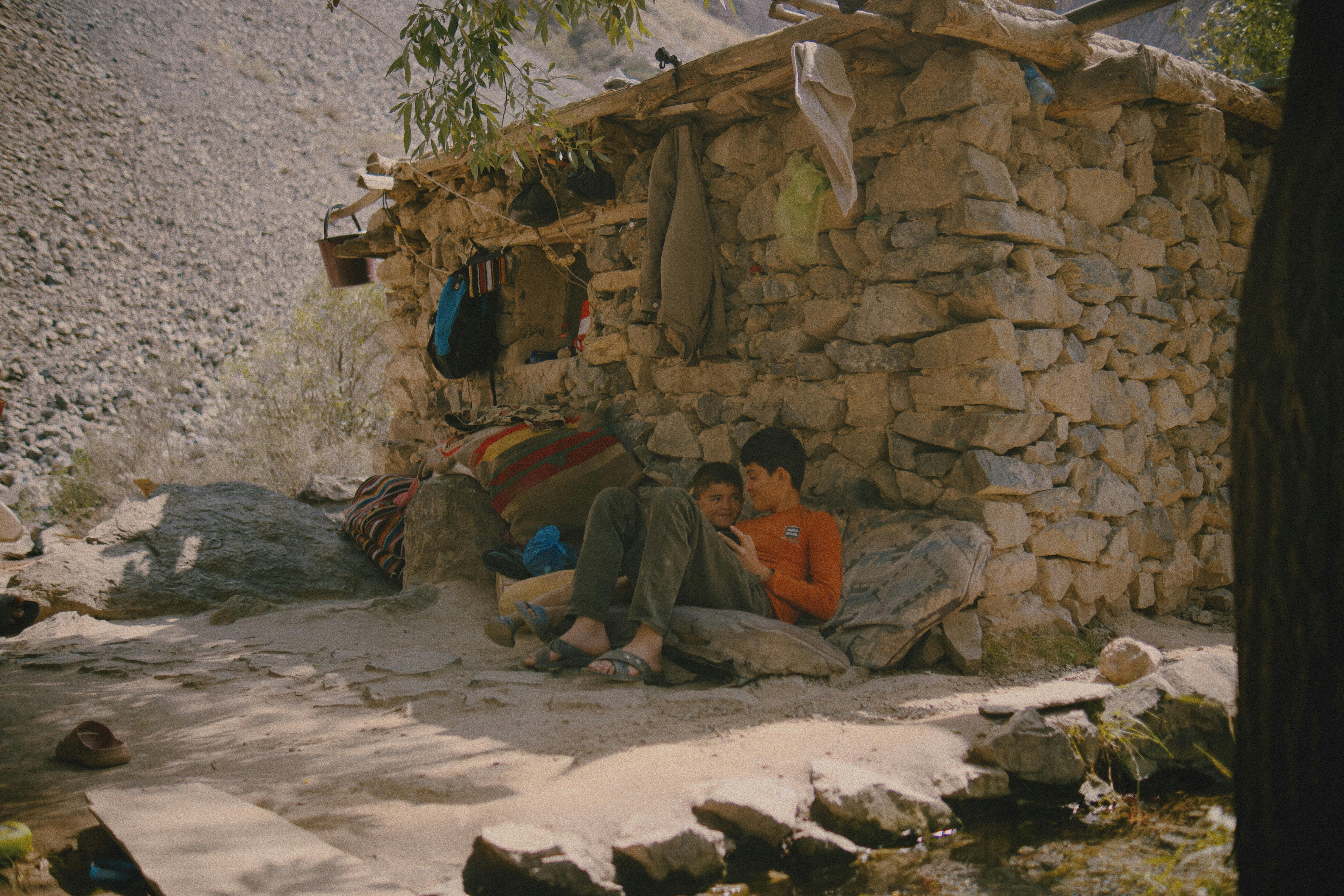 Two children resting on cushions against a rustic stone wall in a mountain landscape