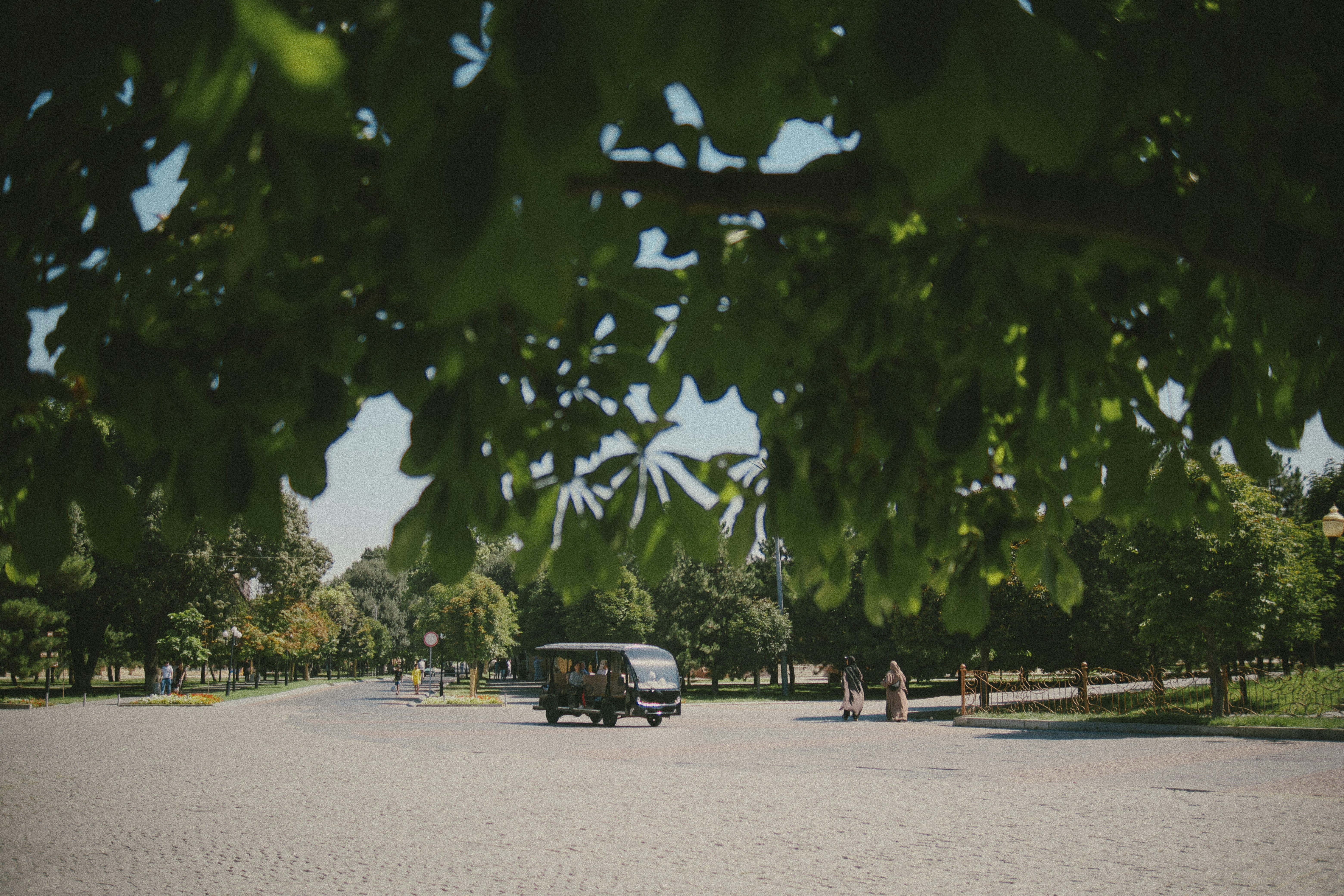 A small electric shuttle driving through a park with trees and paved paths