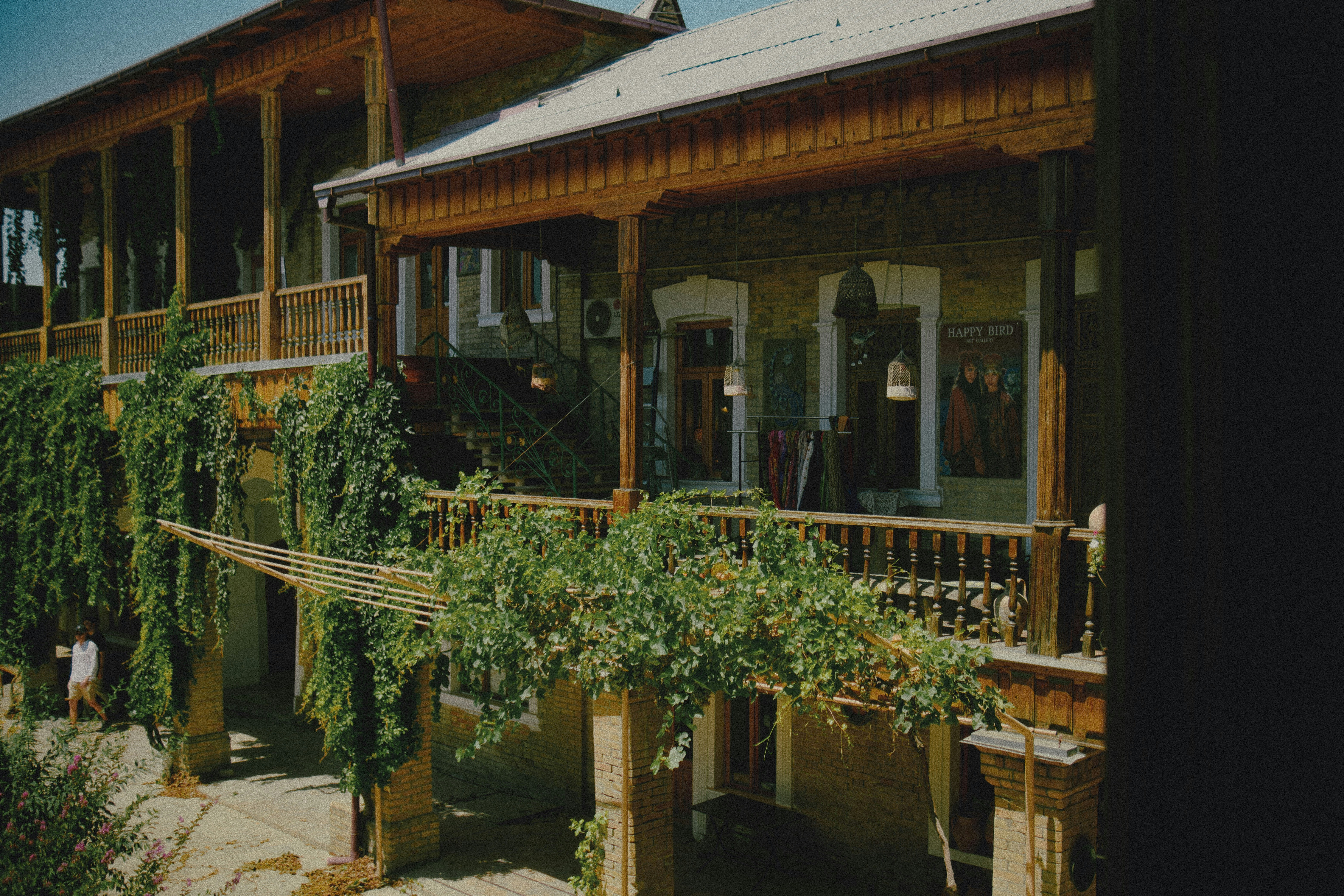 A two-story wooden building with a balcony and climbing vines in a courtyard