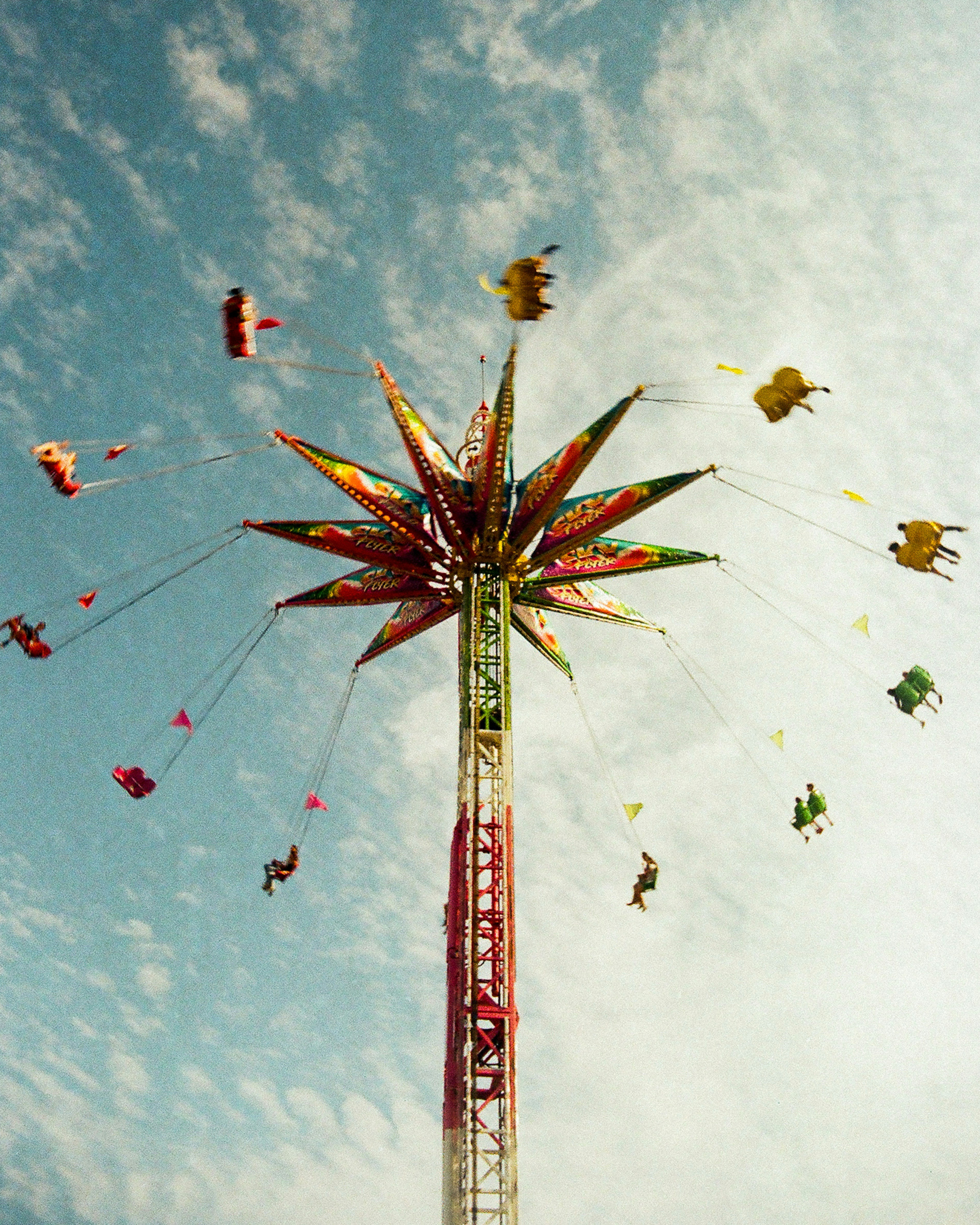 A tall swing ride spinning people in the air against a cloudy sky