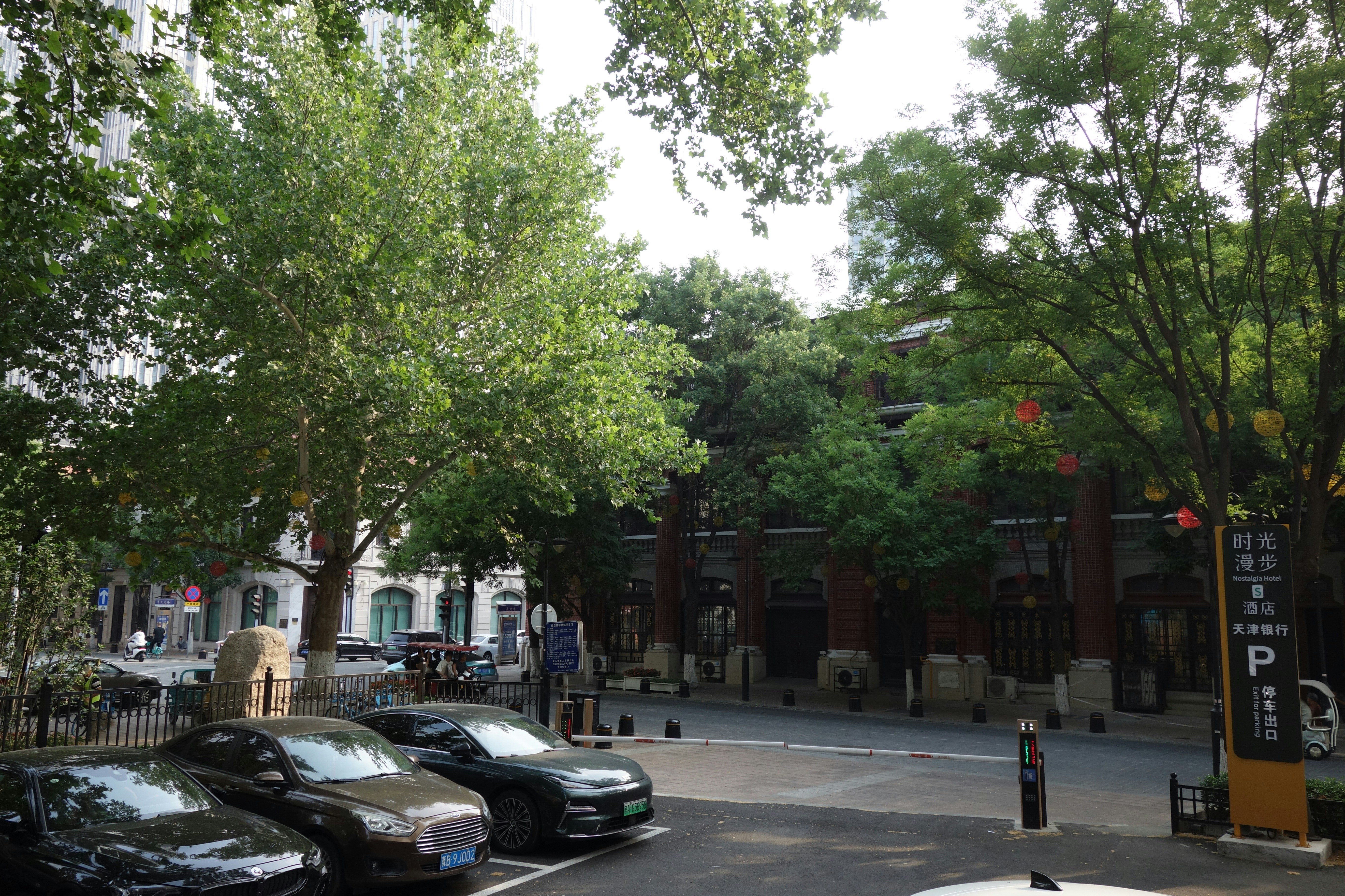 Cars parked near a brick building with trees and a parking sign in Tianjin