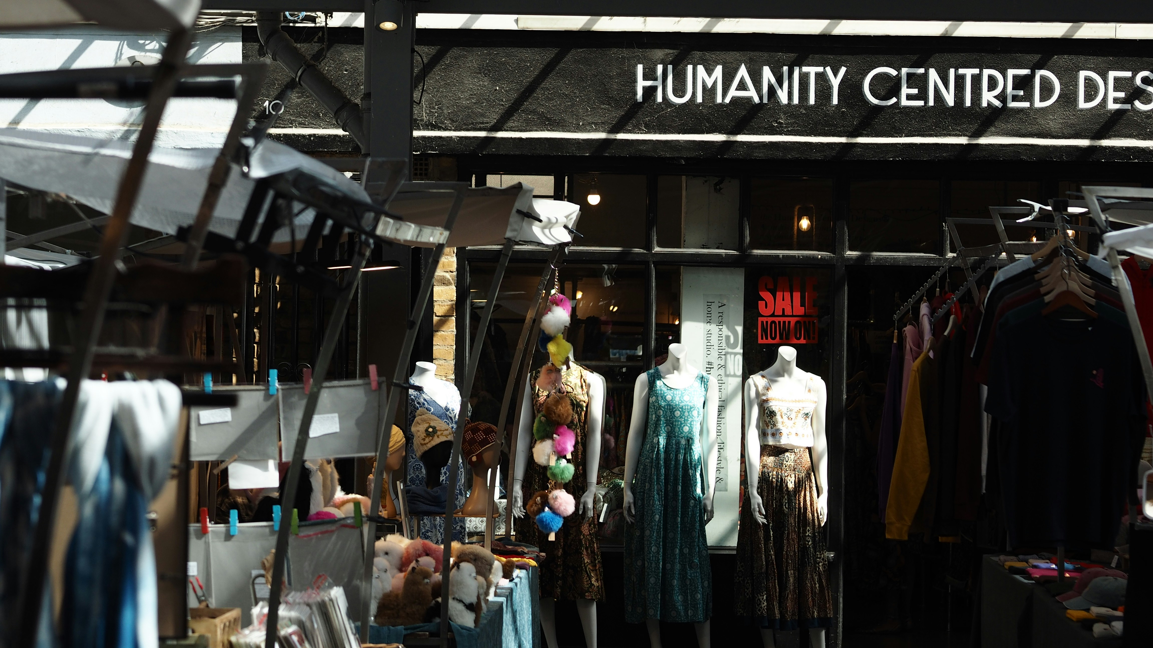 Mannequins wearing dresses in front of a shop with a sign reading HUMANITY CENTRED DESIGN