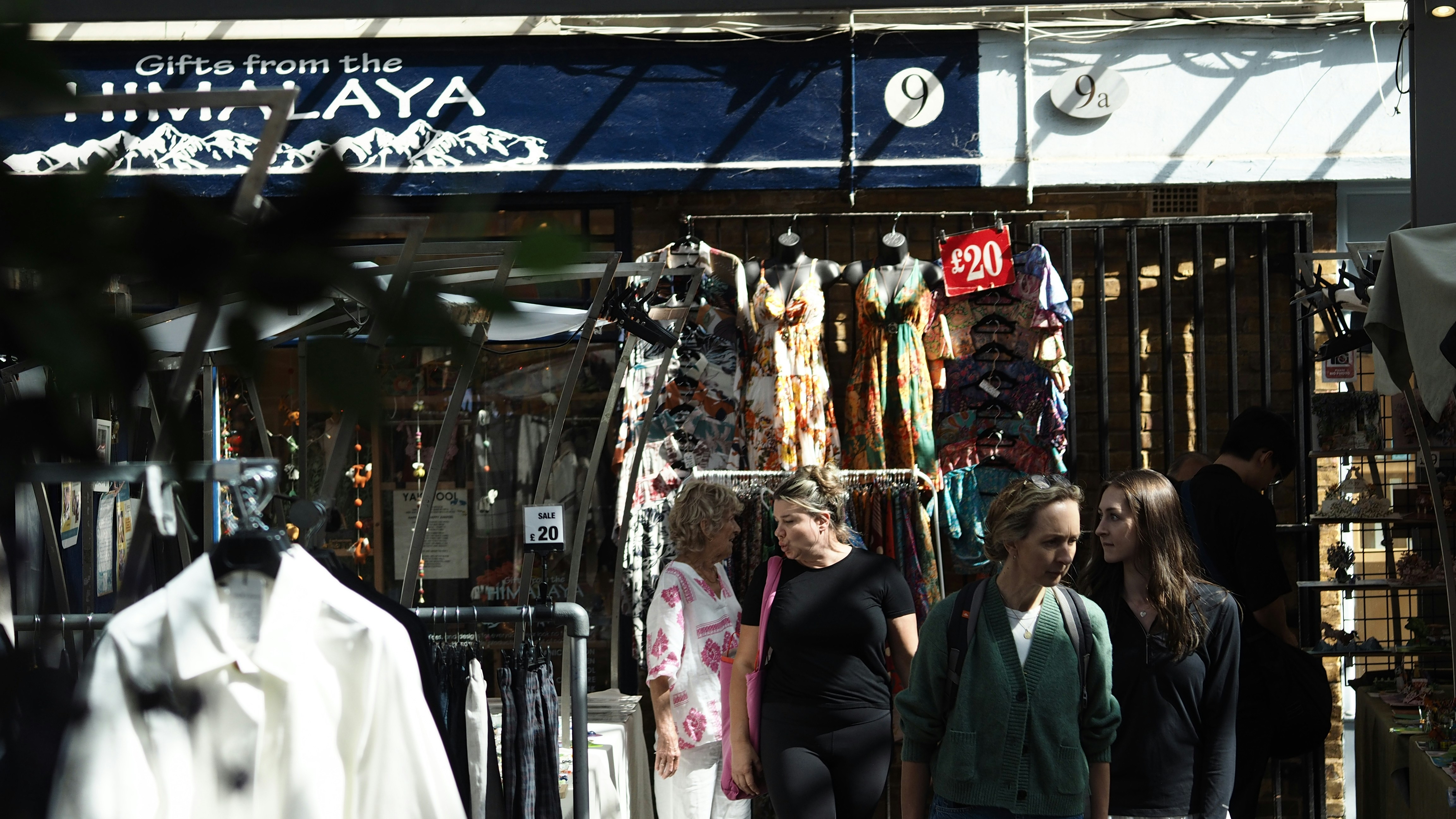 People walking past a clothing shop with dresses displayed on mannequins in a market