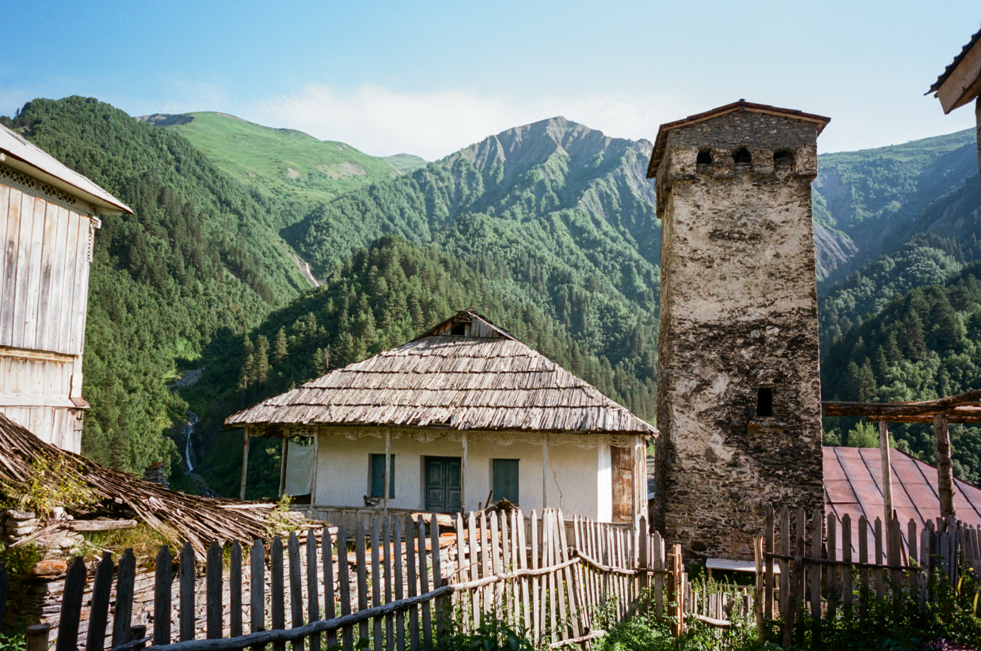 An old Svan defensive tower beside a village house in a wooded Svaneti valley