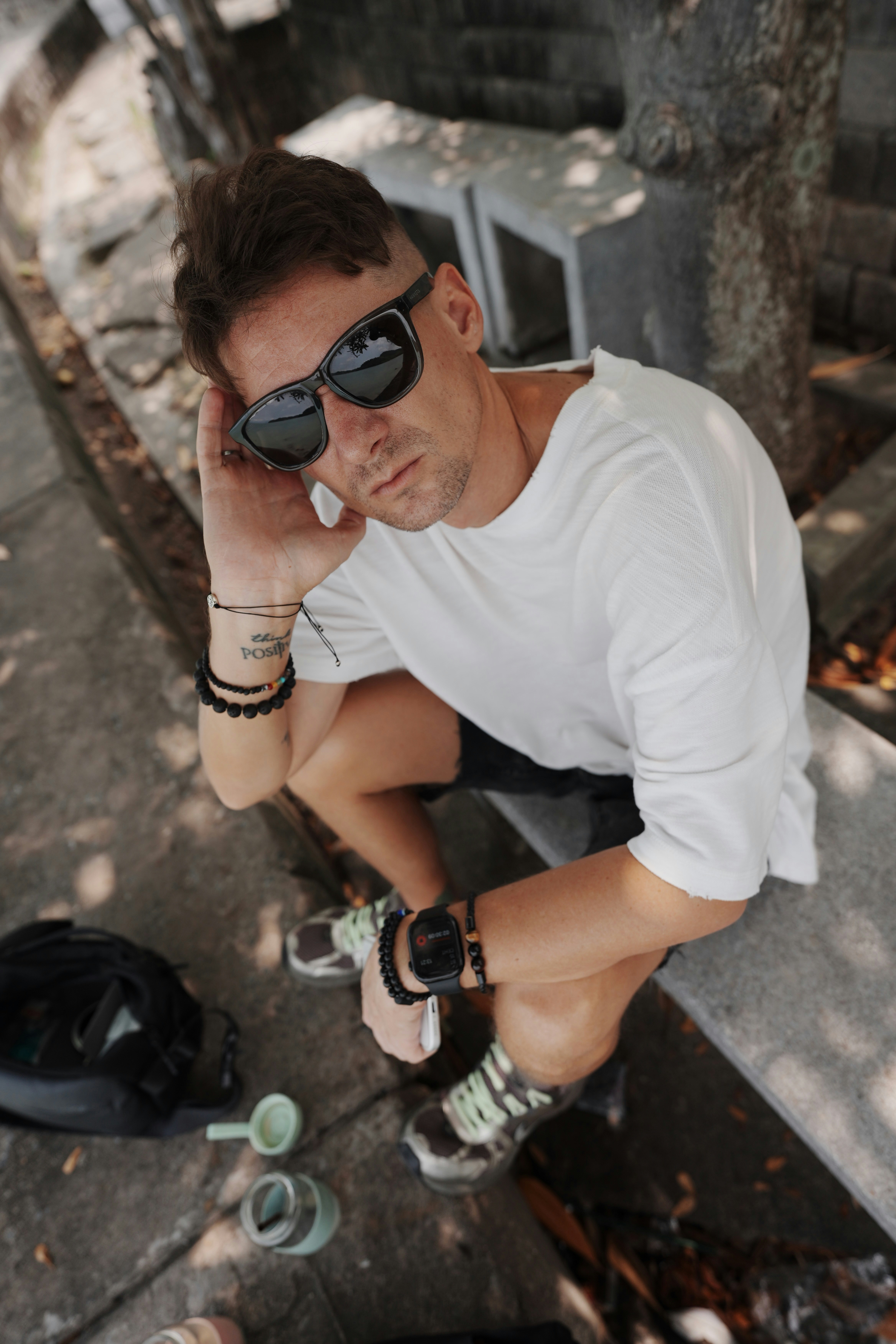 A man in a white t-shirt and sunglasses sitting on a stone bench