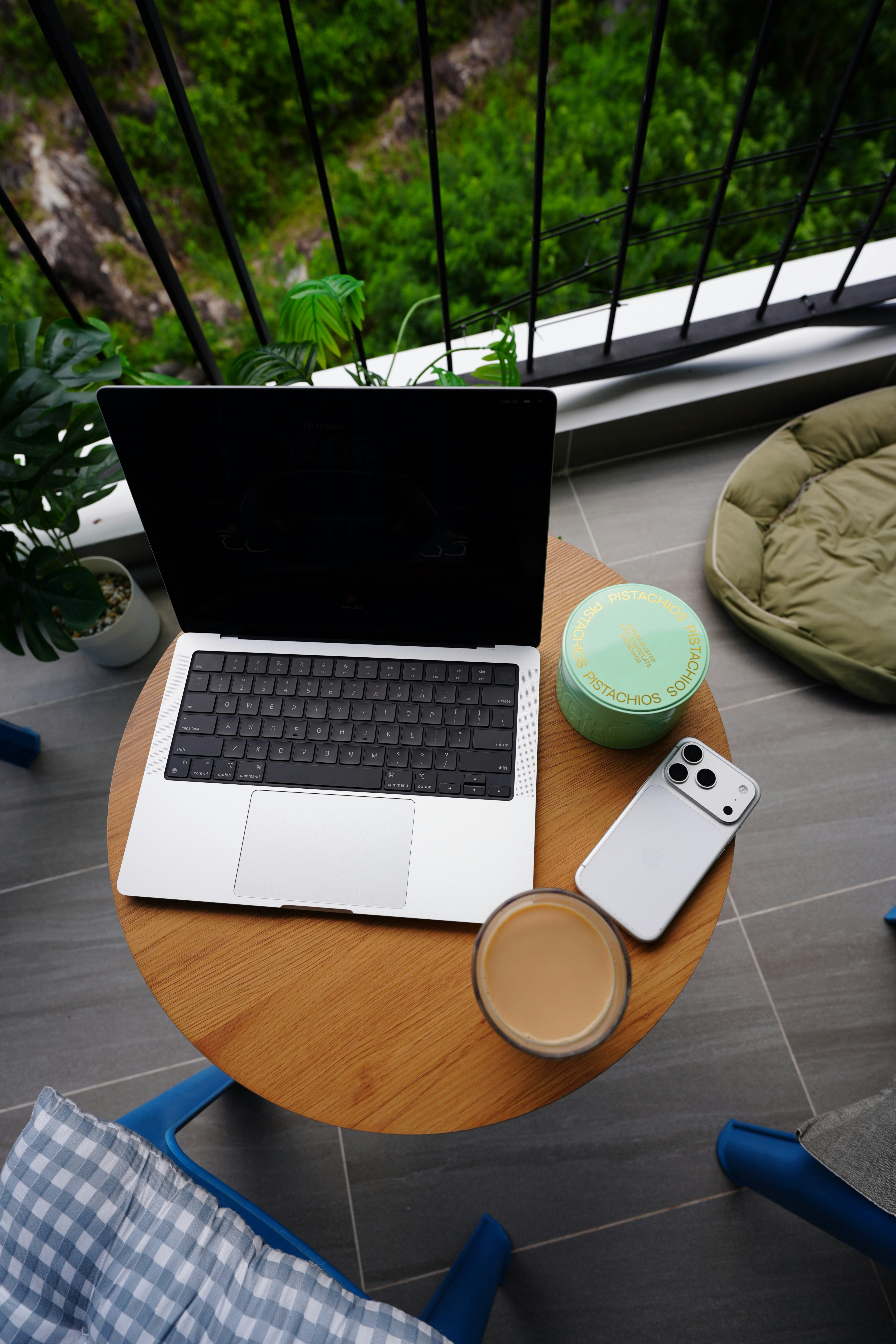 A laptop, smartphone, and coffee on a round wooden table on a balcony