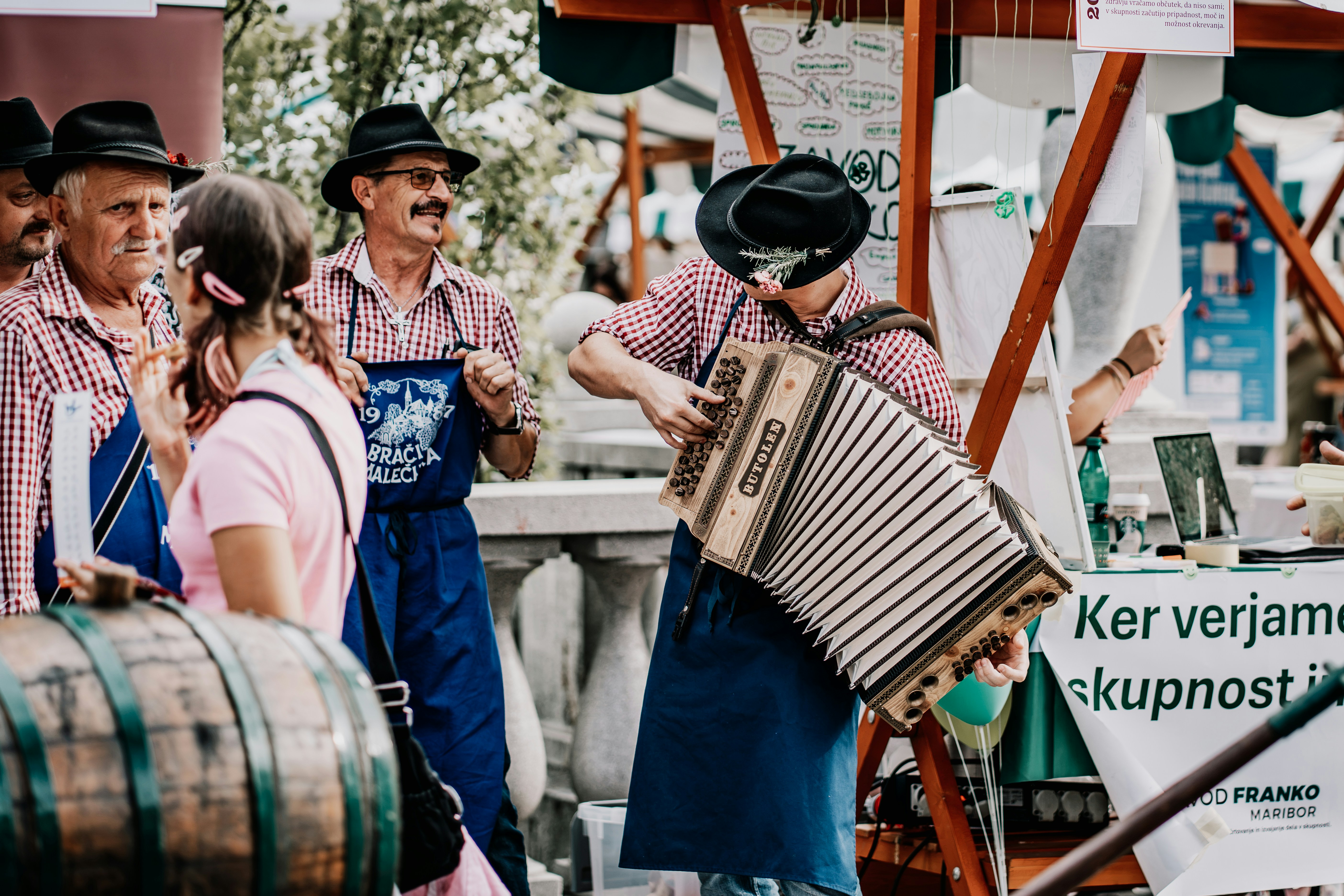 A man playing an accordion while wearing a hat and apron at a market