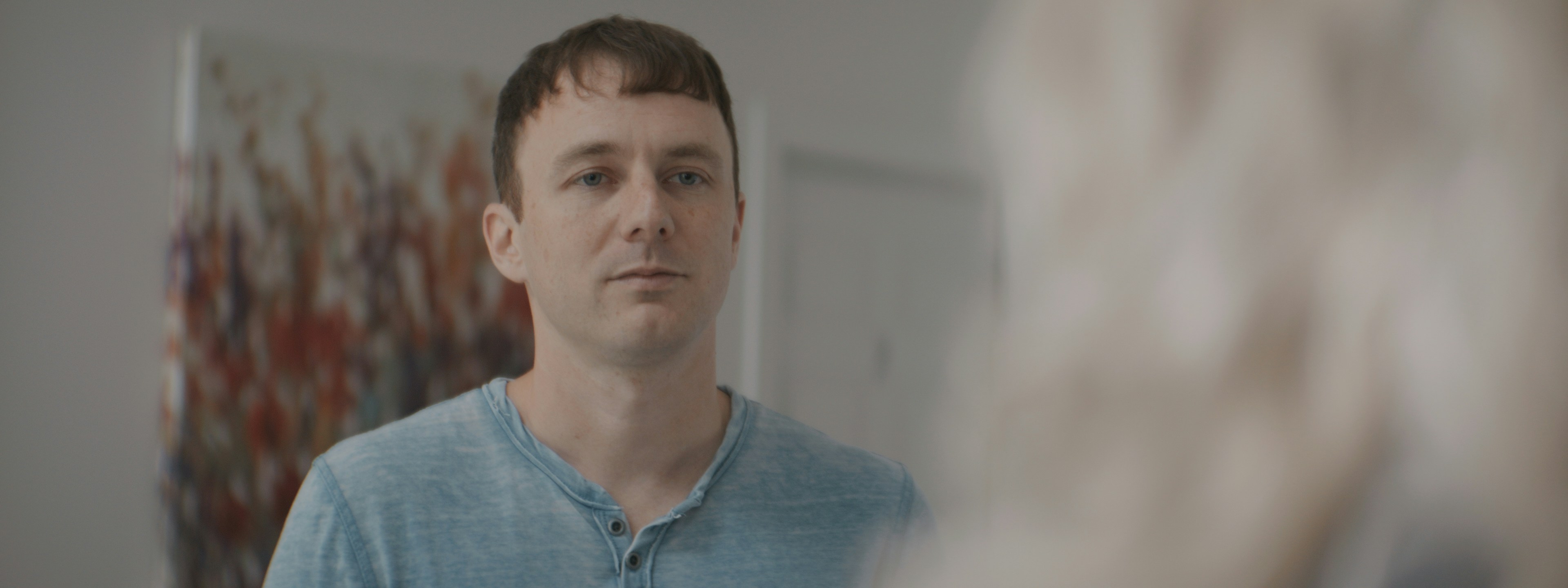 A man in a blue t-shirt looking toward a blurred person in the foreground