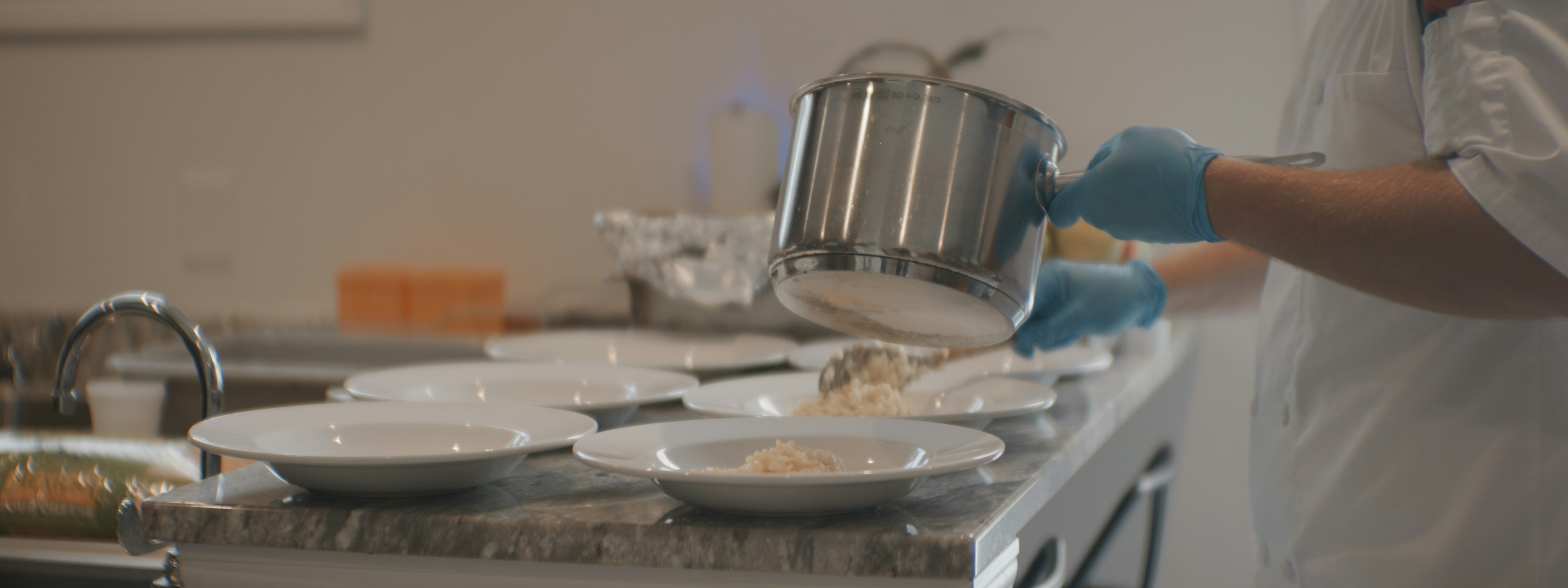 A chef in a white uniform and blue gloves plating rice into white bowls