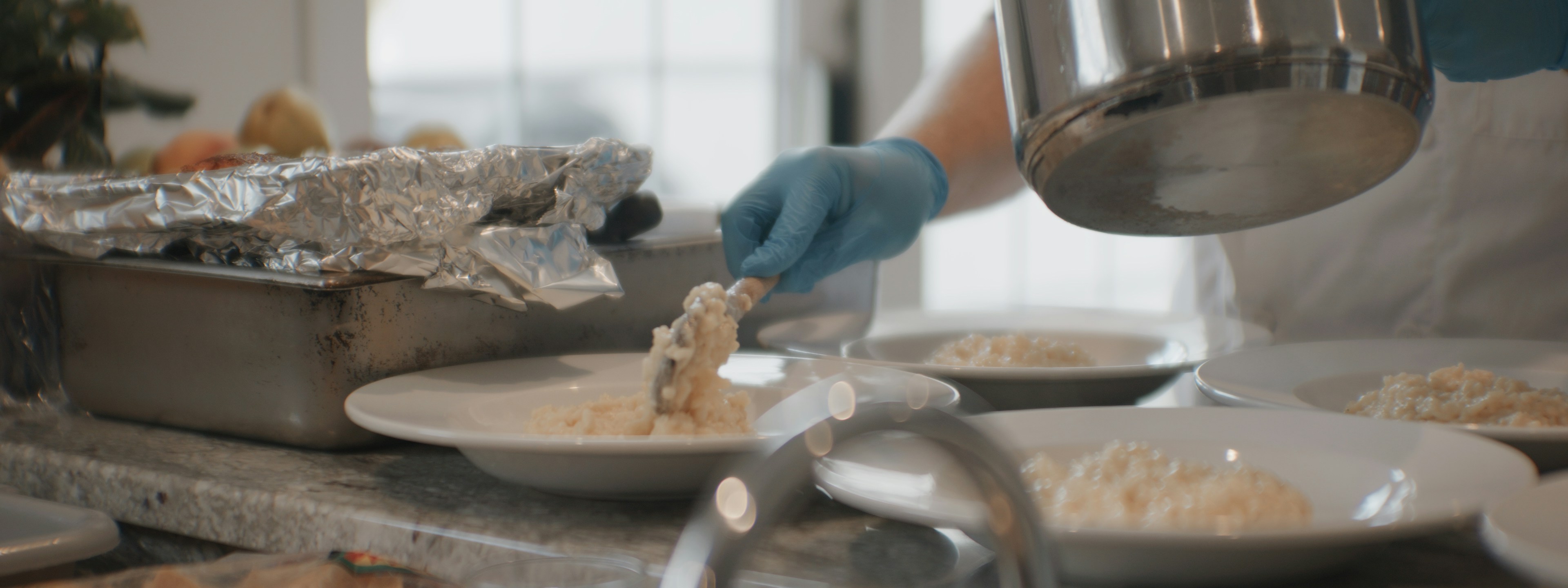 A person in blue gloves plating risotto into white bowls in a kitchen