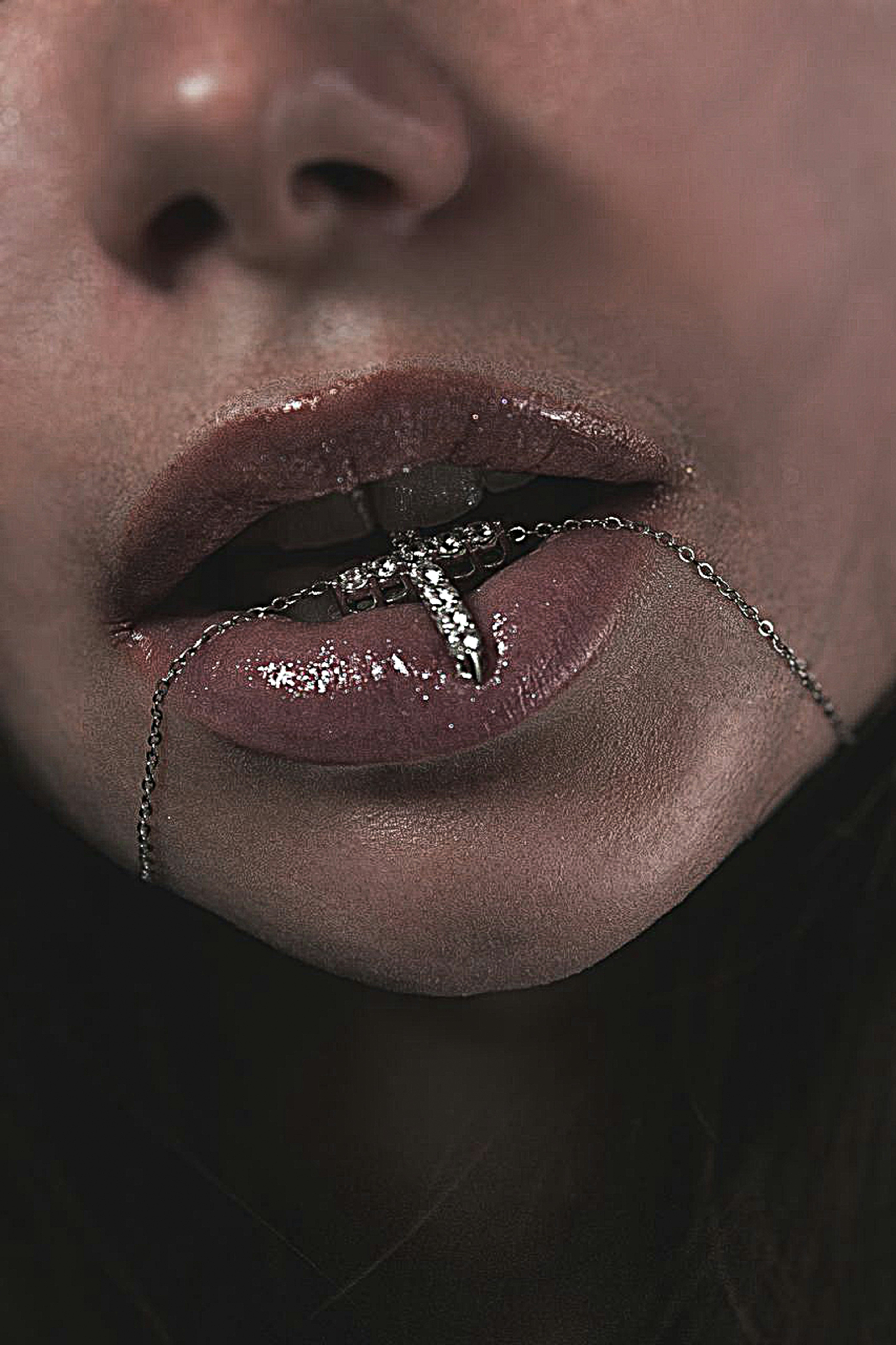 A person holding a silver cross necklace between their glossy lips