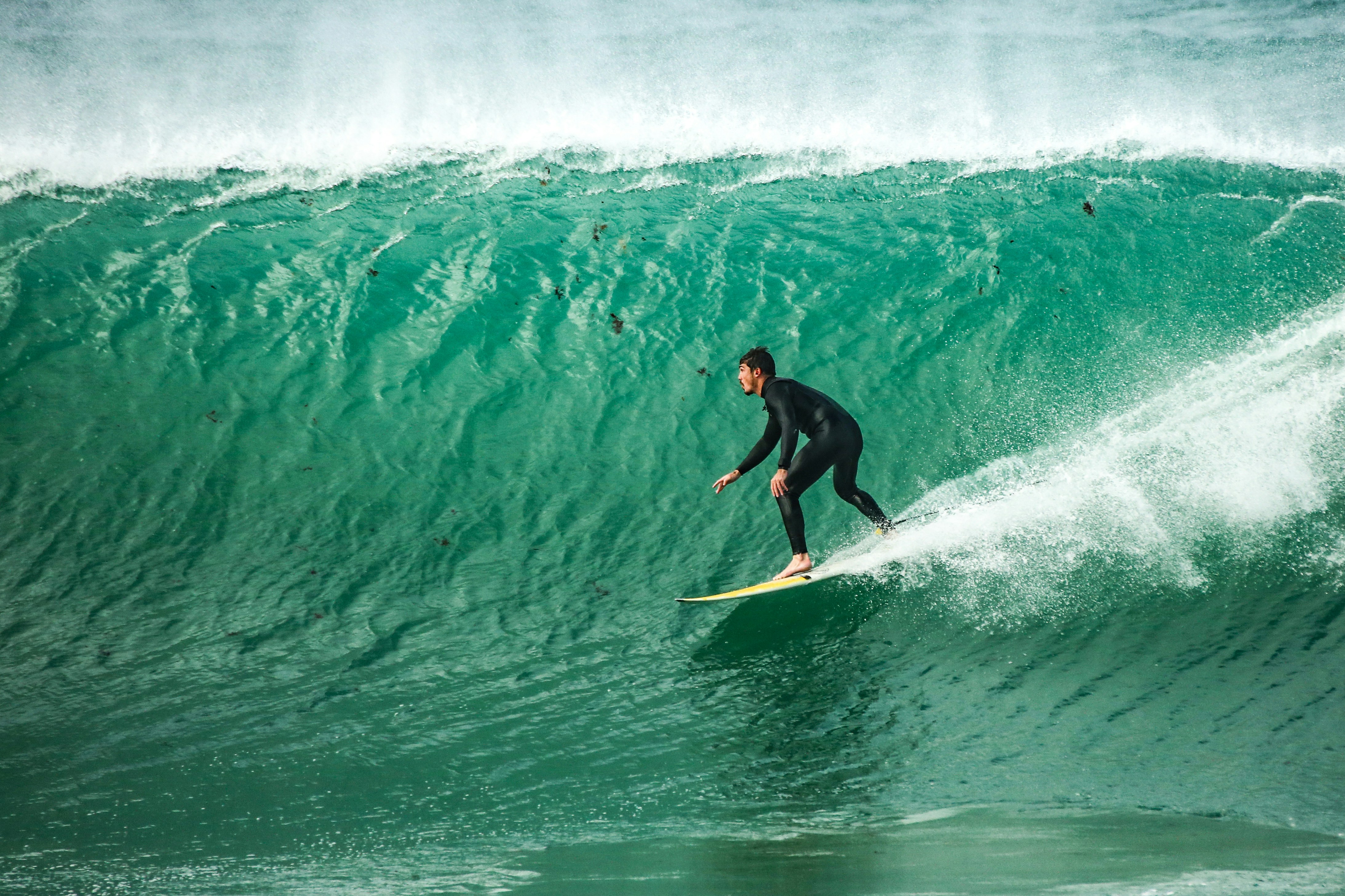 A surfer in a black wetsuit riding a large turquoise ocean wave